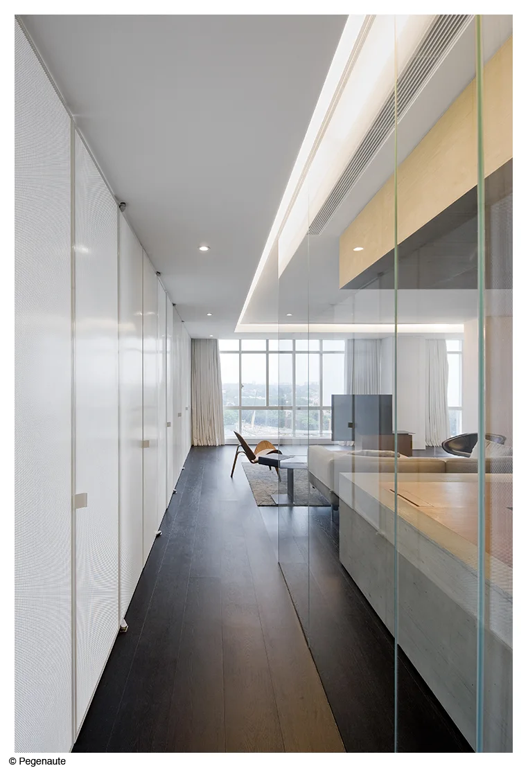 A modern hallway with dark wood flooring, a long wall of white built-in storage cabinets, and a transparent glass partition.