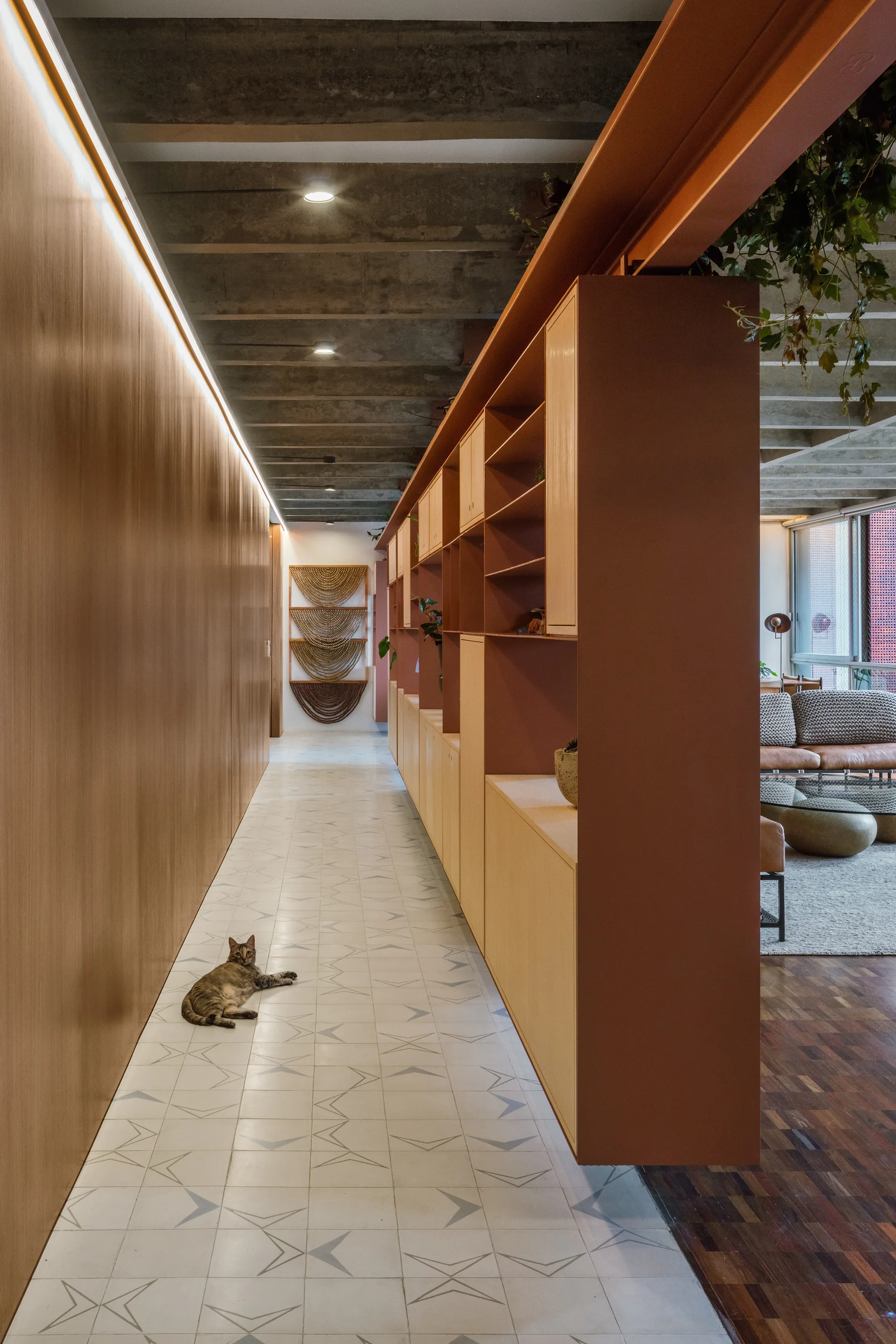 A long hallway features a terracotta-colored room divider, wood paneling with LED strip lighting, and a patterned tile floor leading to a living room.