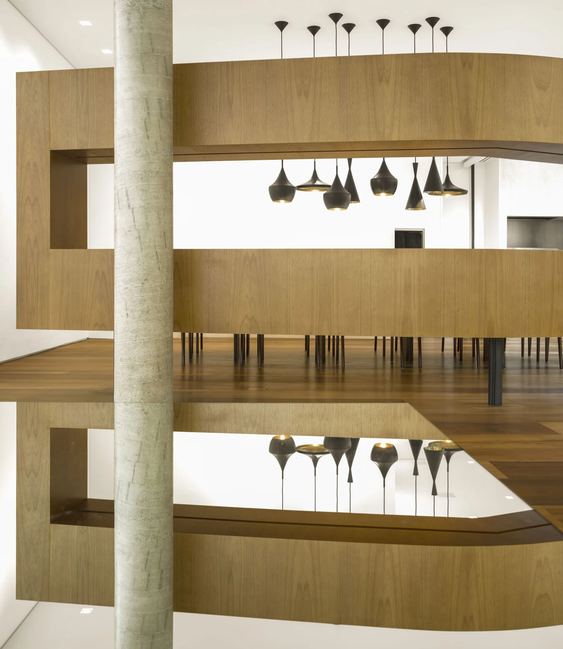 A curved wood partition divides a modern room featuring a stone column, several black pendant lights, and a highly reflective polished floor.