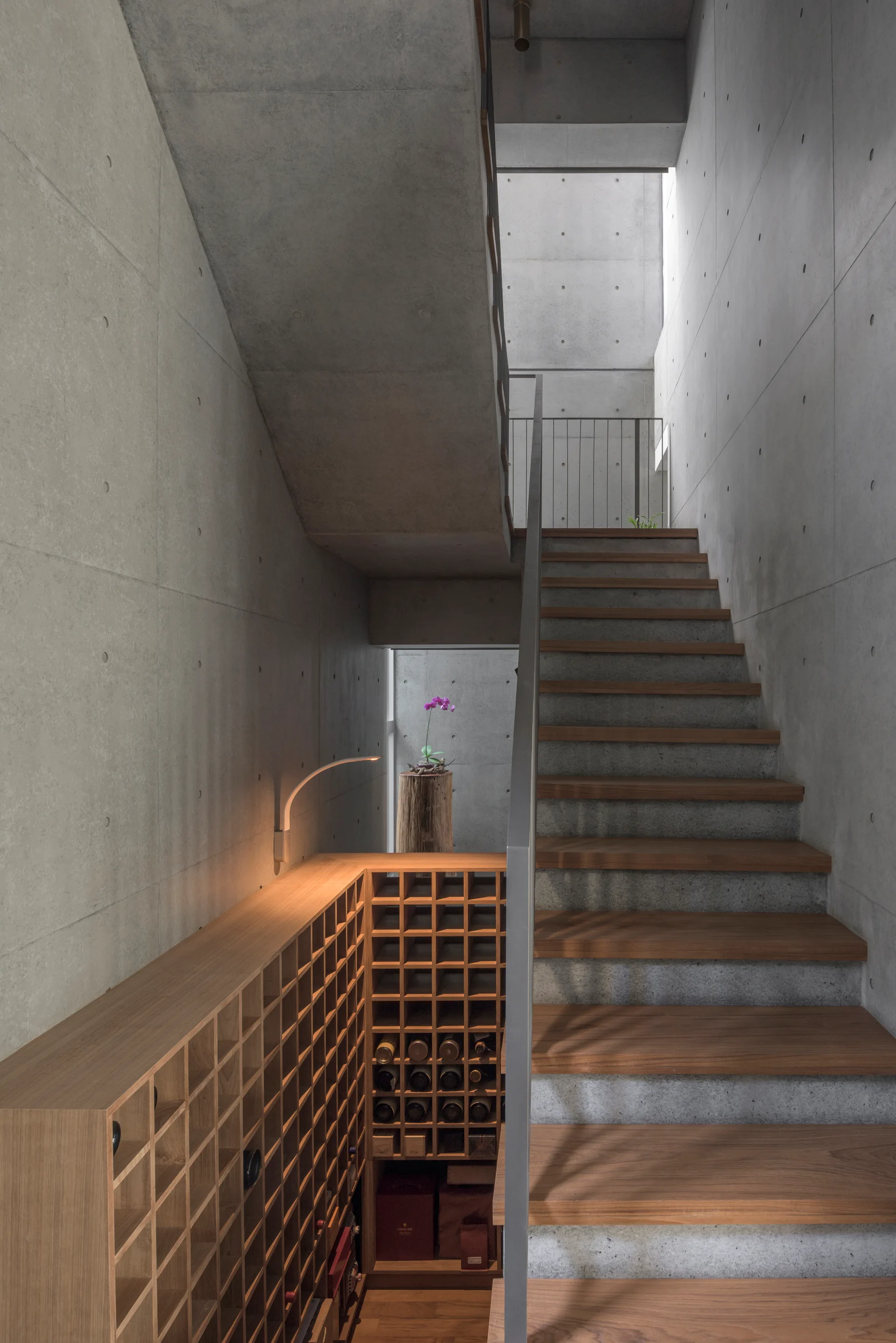 A modern wooden staircase with exposed concrete walls features a custom wooden wine cubby system integrated underneath the steps.