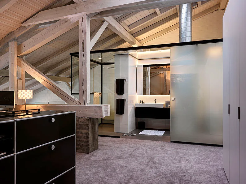 A modern attic loft bathroom featuring a black vanity, glass enclosure, and prominent exposed wooden ceiling beams.