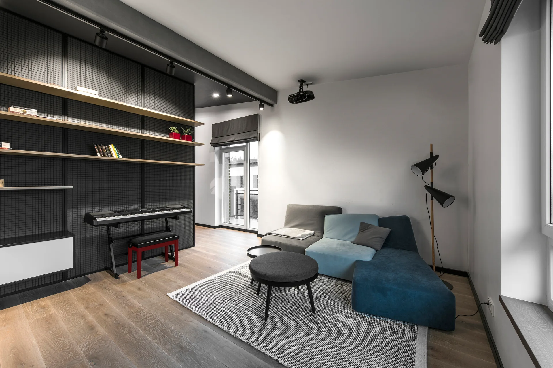 A modern living room features a blue modular sofa, a dark metal grid wall shelving unit with a keyboard, and light wood flooring.