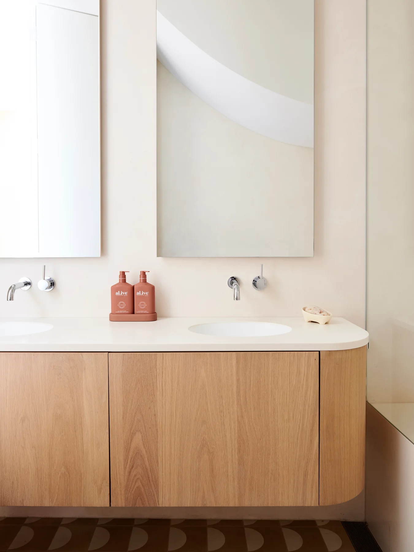 A light wood bathroom vanity with rounded corners, integrated double sinks, wall-mounted chrome faucets, and two rectangular mirrors.
