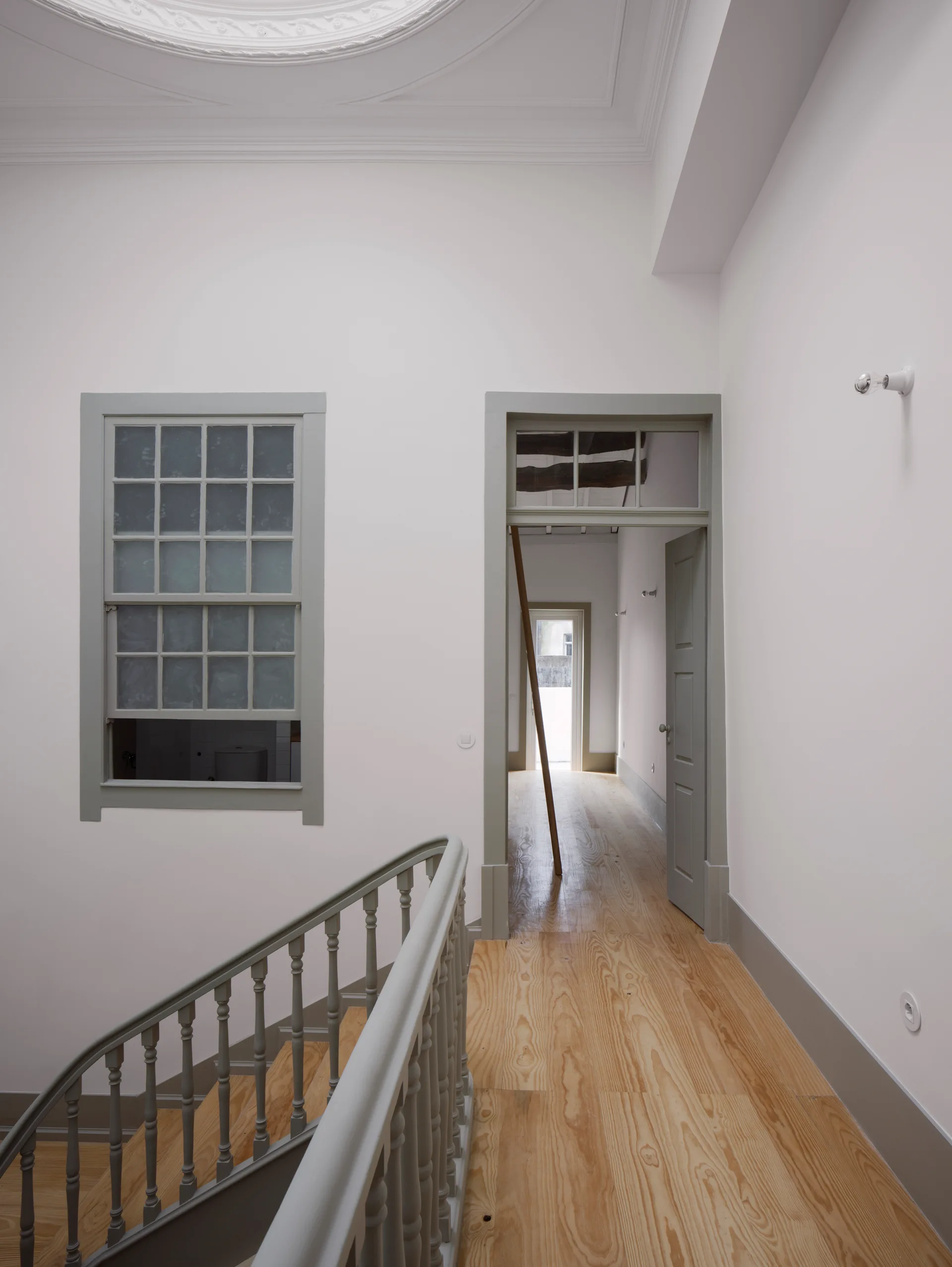 An interior landing features a curved staircase with a sage green railing, light wood floors, and matching green painted door trim against white walls.