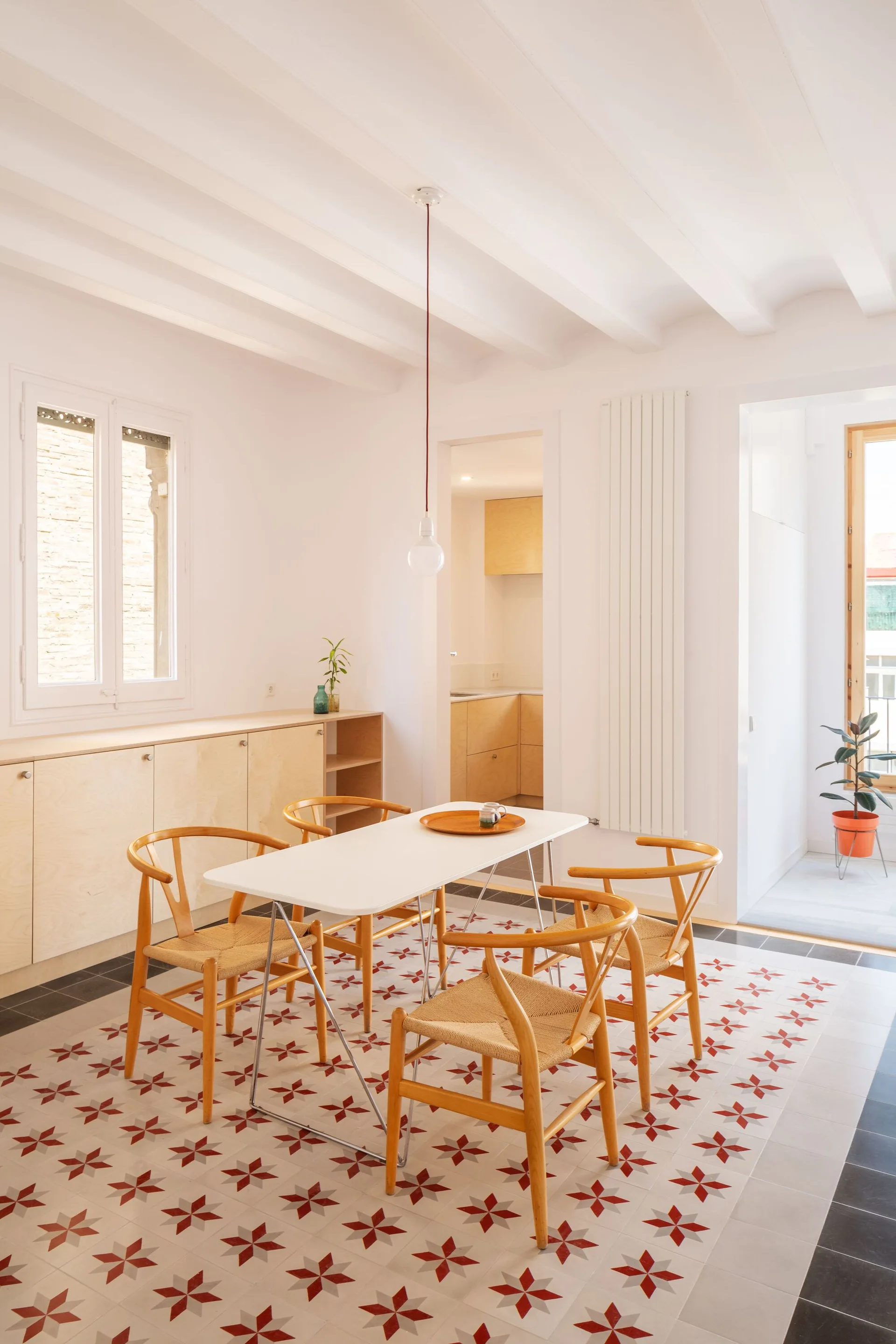 A bright dining room features wooden wishbone chairs around a white table on a red and white geometric star patterned tile floor.
