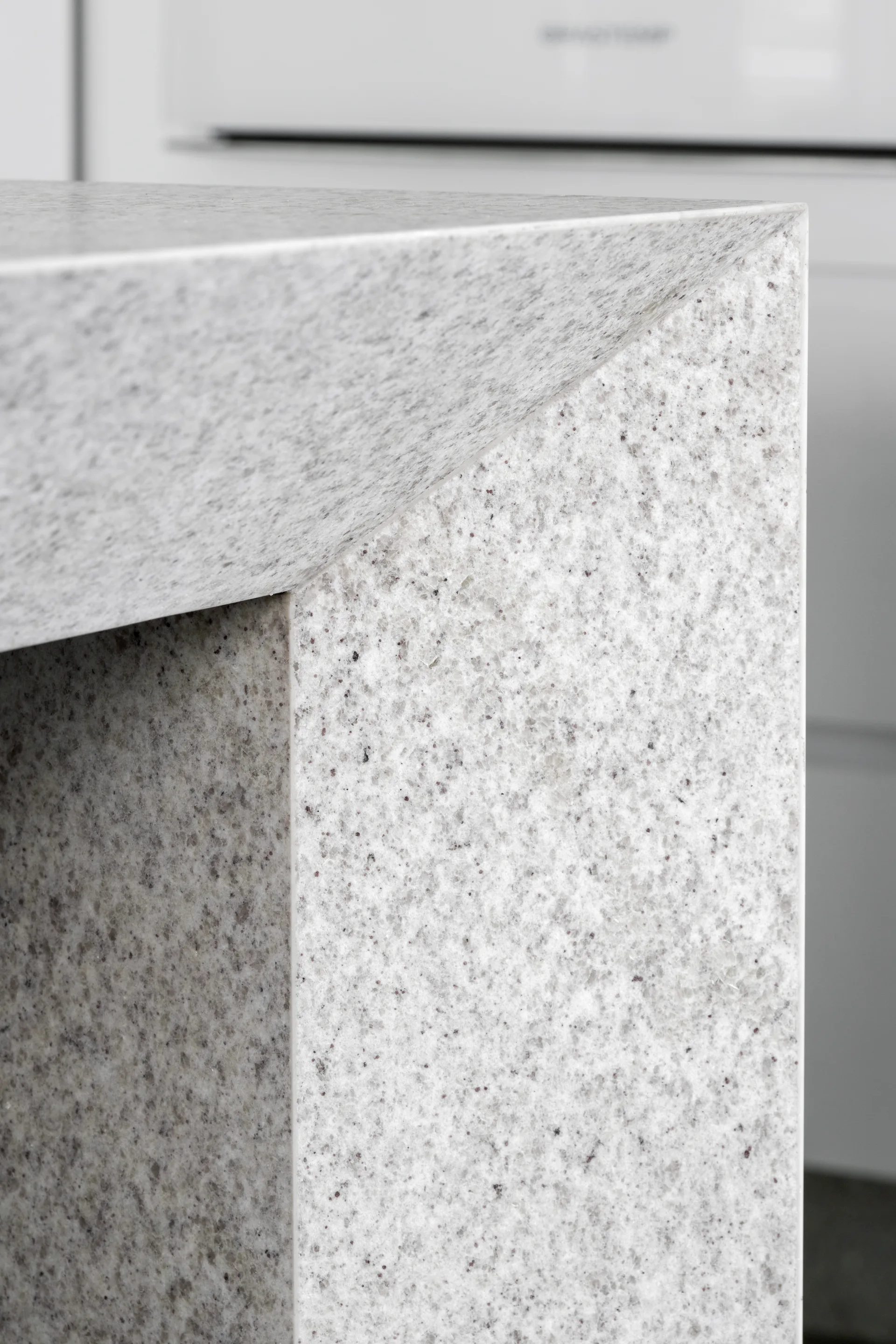 An extreme close-up of a speckled gray stone kitchen countertop corner showing a clean mitered edge profile and a matte finish.