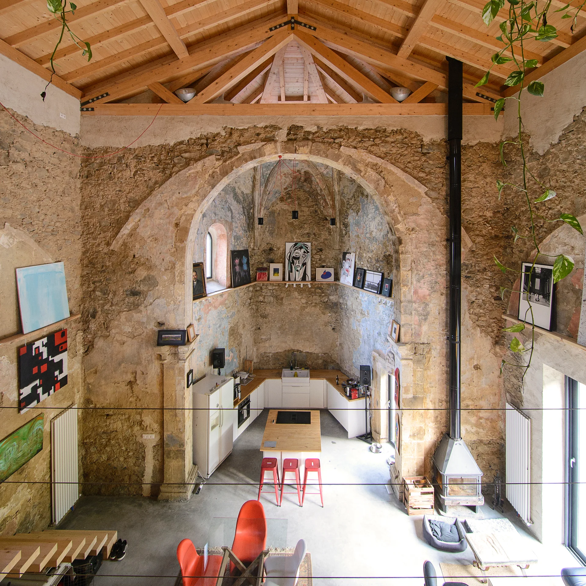 A contemporary white kitchen with a wood-topped island is built under a large historic stone arch with high timber ceilings.