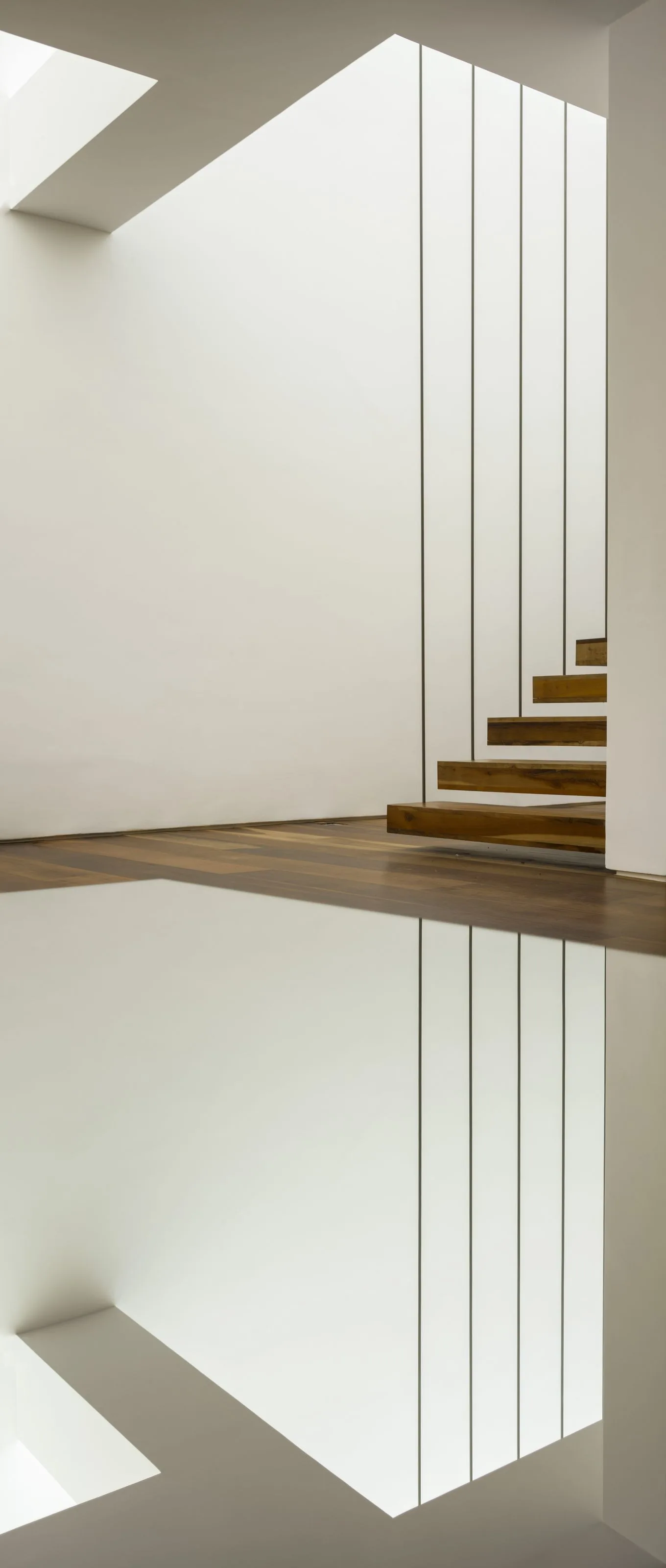 A minimalist staircase features floating wood treads and vertical metal cable railings set against a plain white wall and wood flooring.