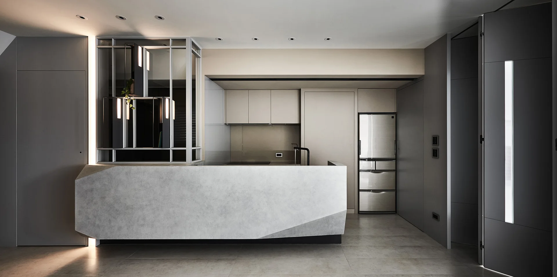 A minimalist grey kitchen with a large sculptural stone-like island, flat-panel cabinets, and a glass partition with integrated lighting.
