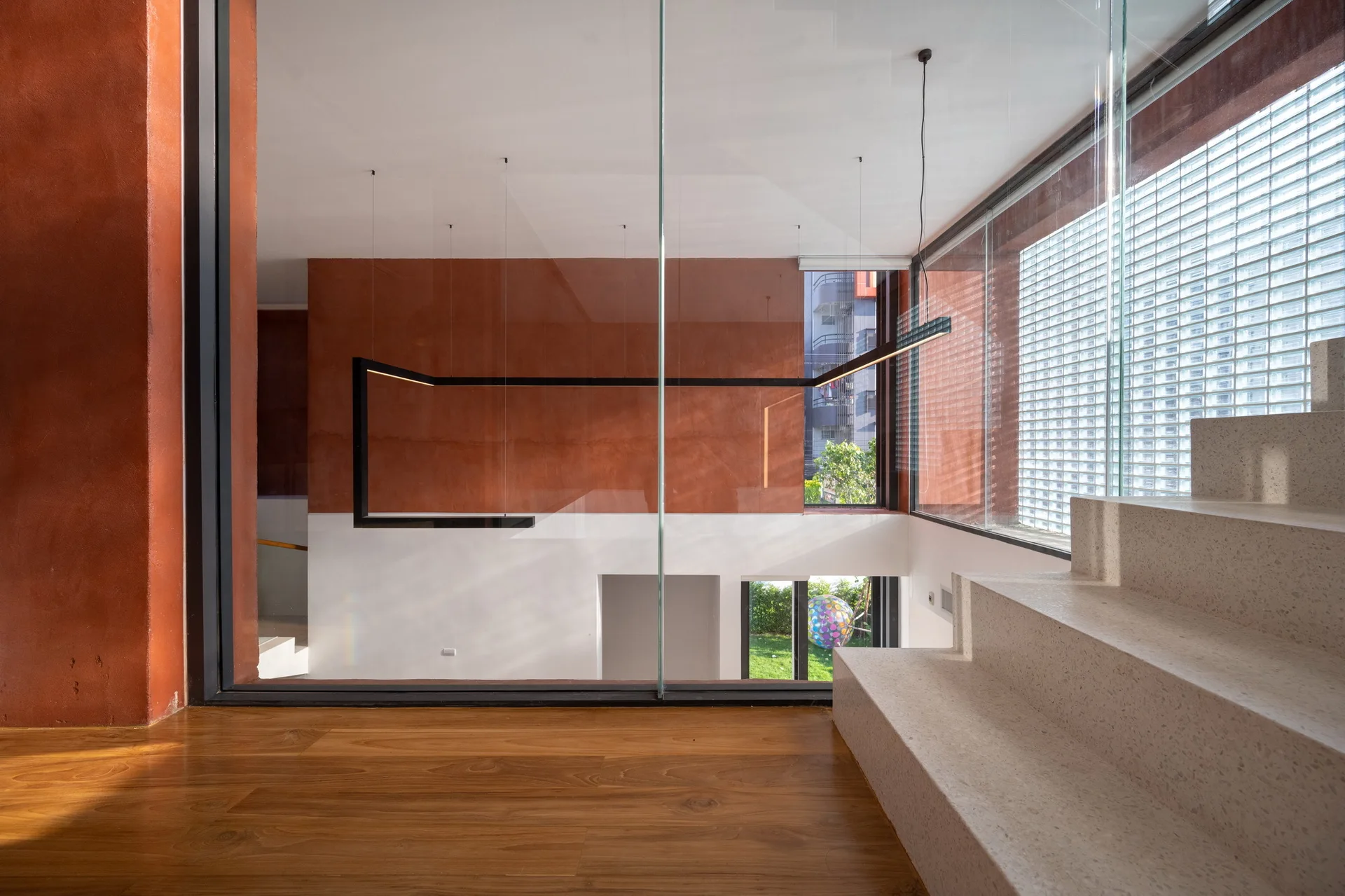 A modern staircase featuring speckled terrazzo treads is set against deep terracotta plaster walls and a large glass partition.