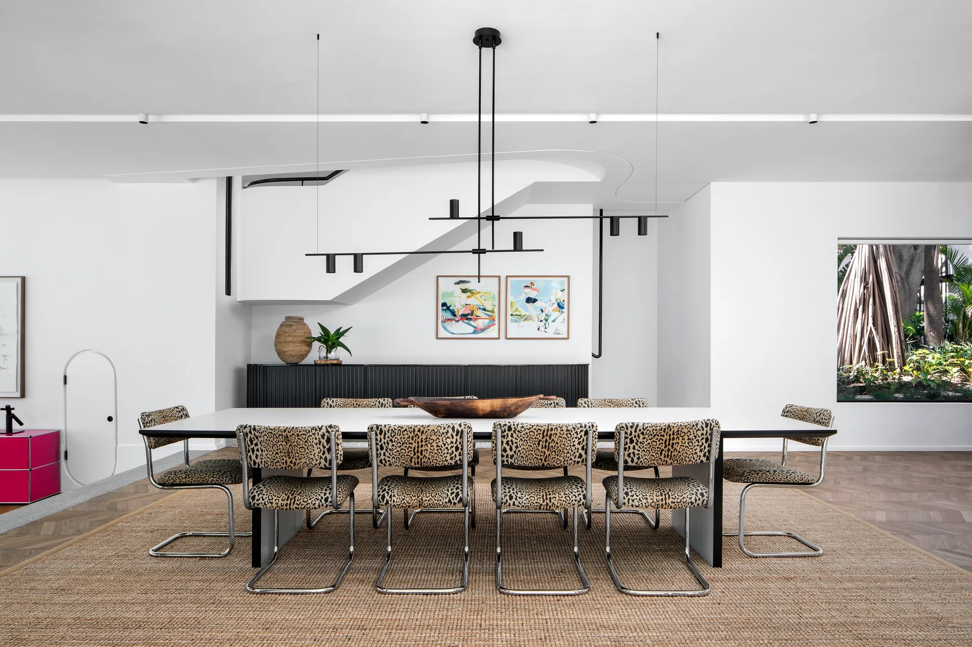 A modern dining room features a white table surrounded by eight leopard-print cantilever chairs on a large textured jute rug.