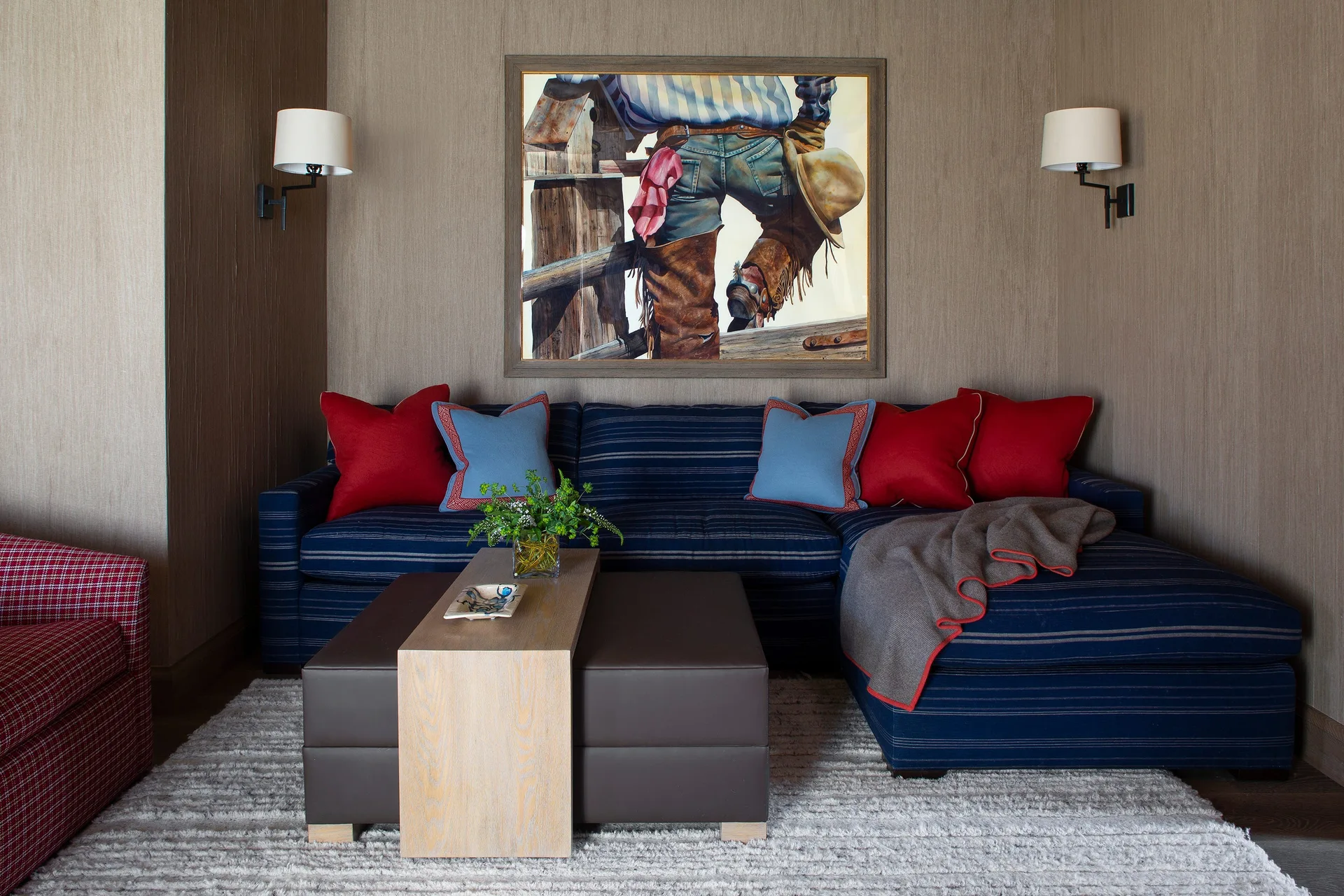 A blue striped sectional sofa sits against a textured brown wall decorated with a cowboy painting and flanked by two white sconces.