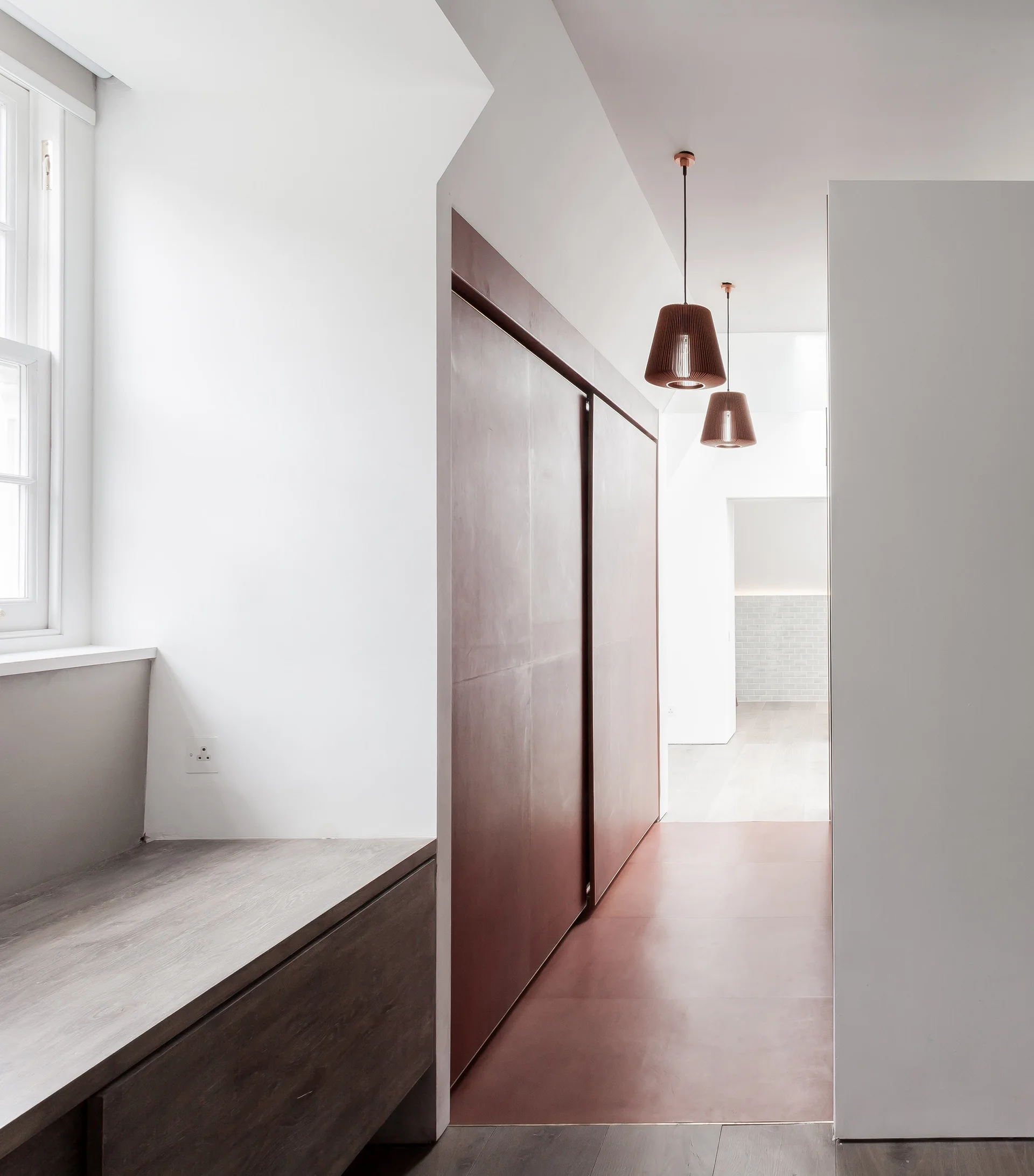 A minimalist hallway features tall reddish-brown sliding doors, matching floor panels, and two copper pendant lights.