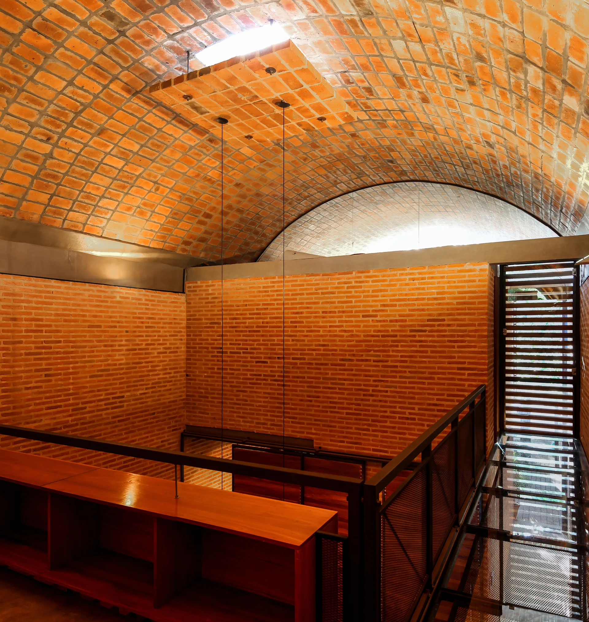 An interior mezzanine features a curved vaulted brick ceiling, red brick walls, a wooden shelving unit, and a black metal grate walkway.