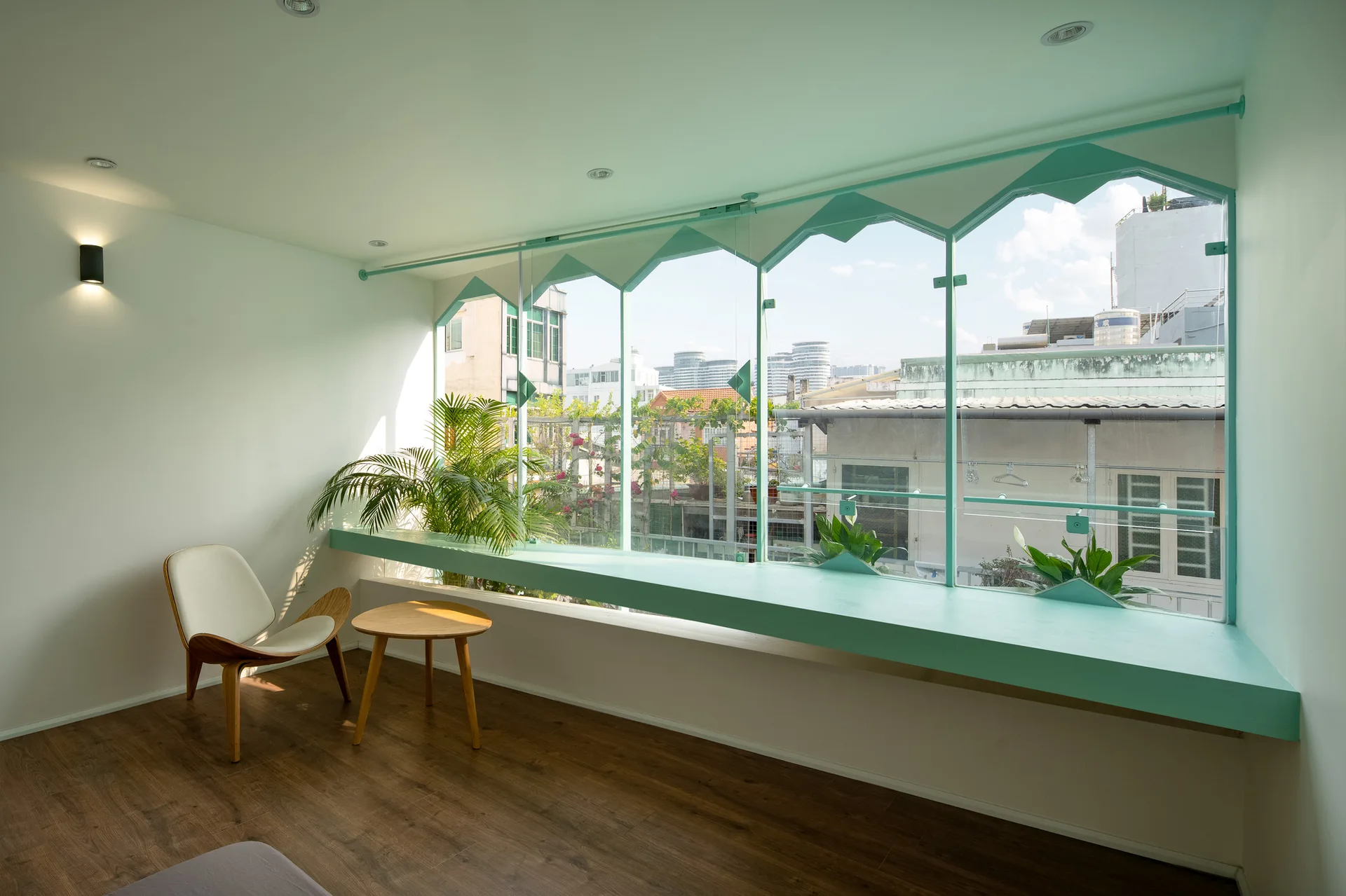 A minimalist room with a wide mint green window sill, a geometric window frame, a mid-century modern chair, and a round wooden side table.