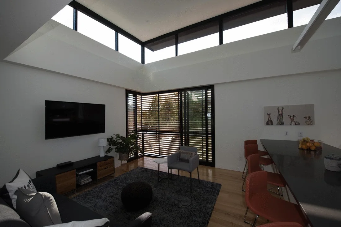 A modern living room features a dark sofa, a grey accent chair, and a high sloped ceiling with clerestory windows letting in natural light.