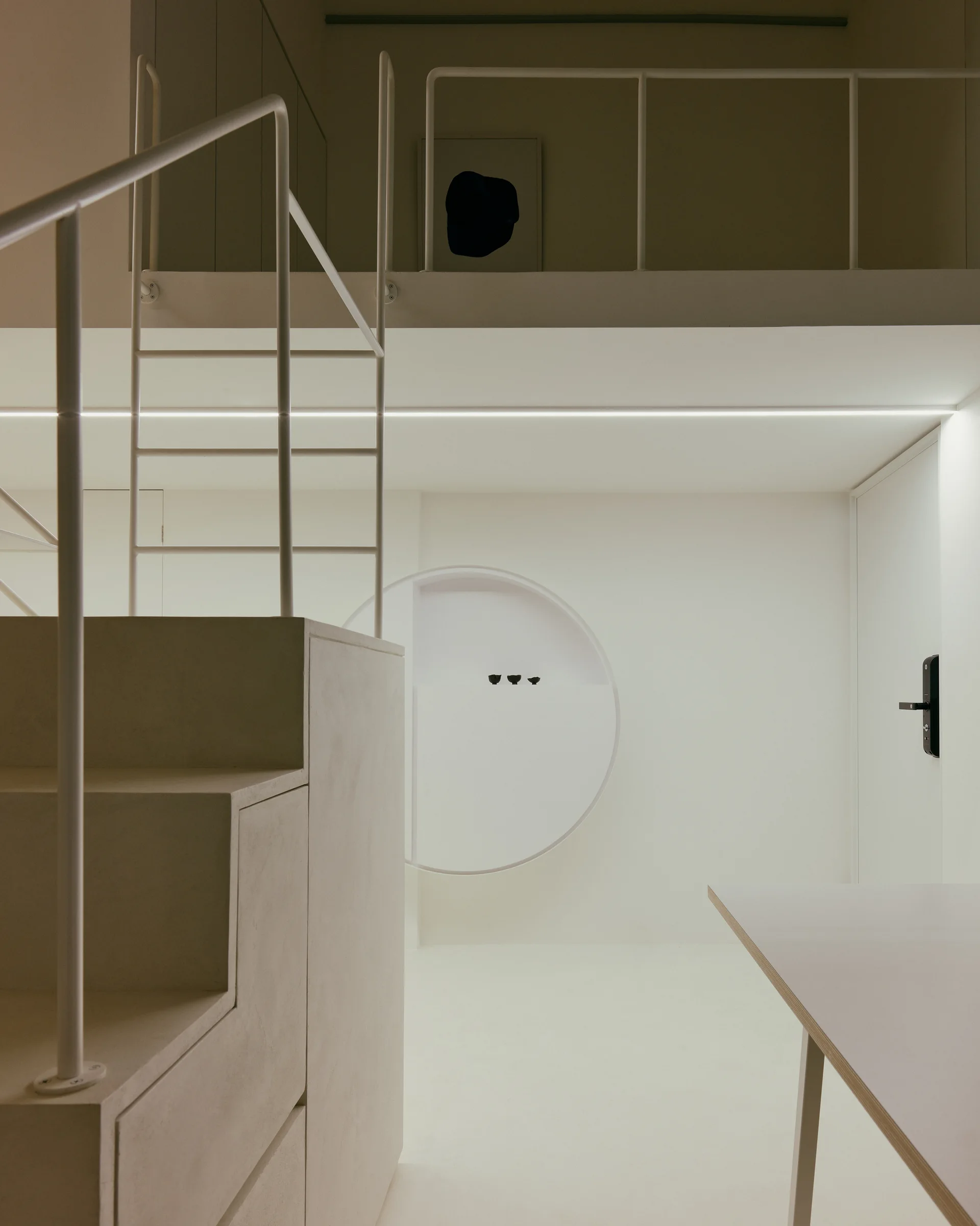 A minimalist cream staircase with integrated storage drawers and thin white railings leads to a mezzanine level next to a circular wall niche.