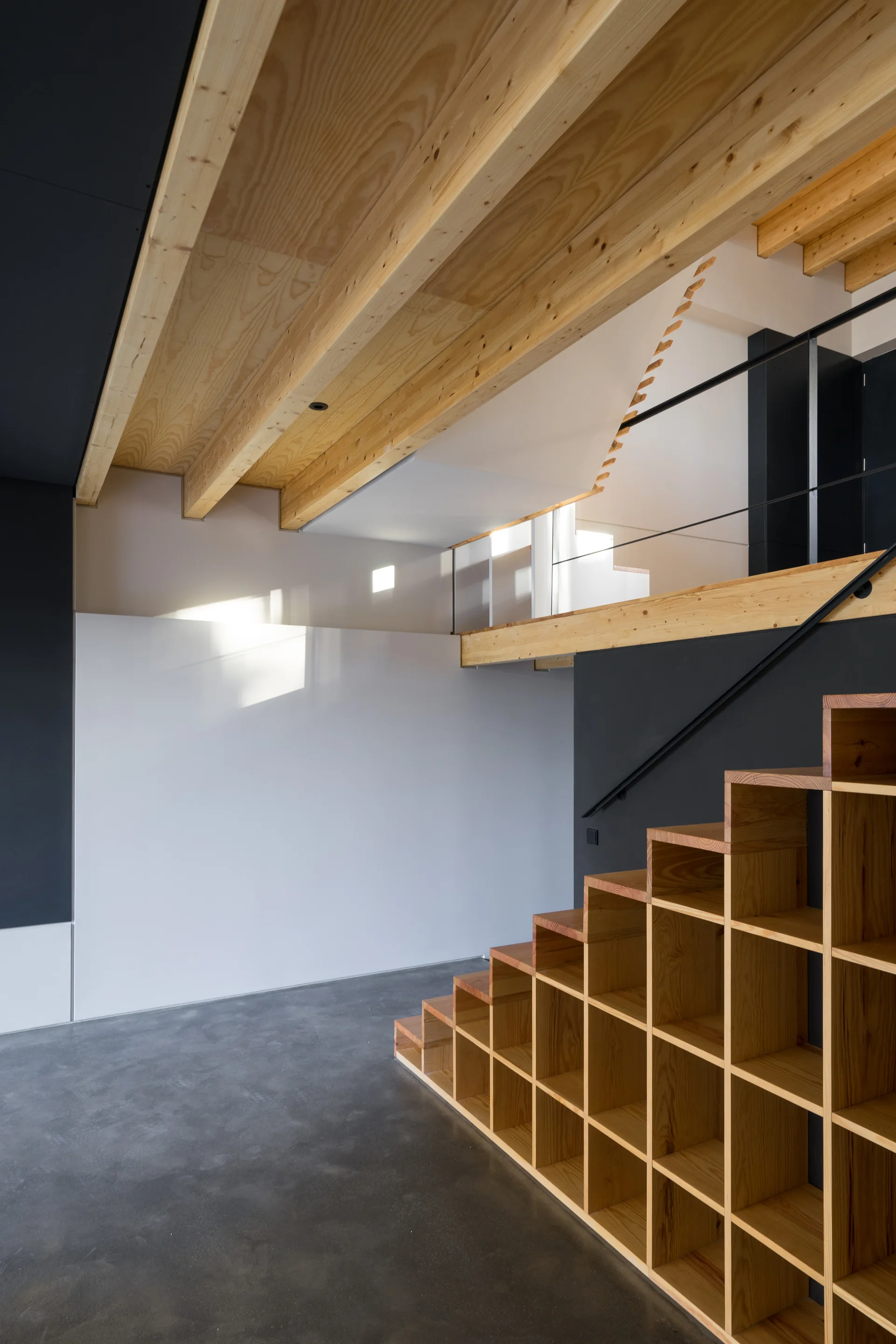 A modern wooden staircase with built-in grid storage cubbies underneath features an exposed timber ceiling and a polished concrete floor.