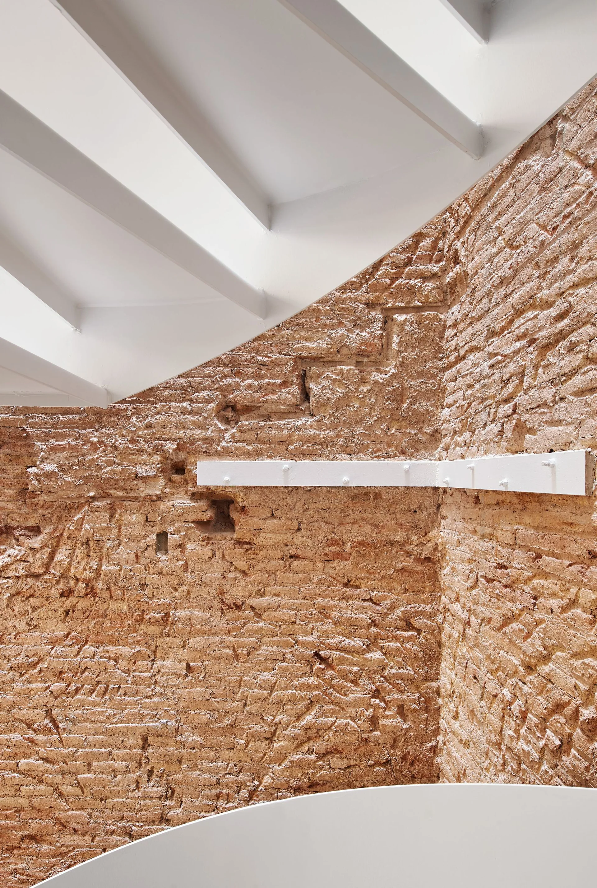 An architectural interior view showing textured terracotta brick walls meeting clean-lined white ceiling beams.