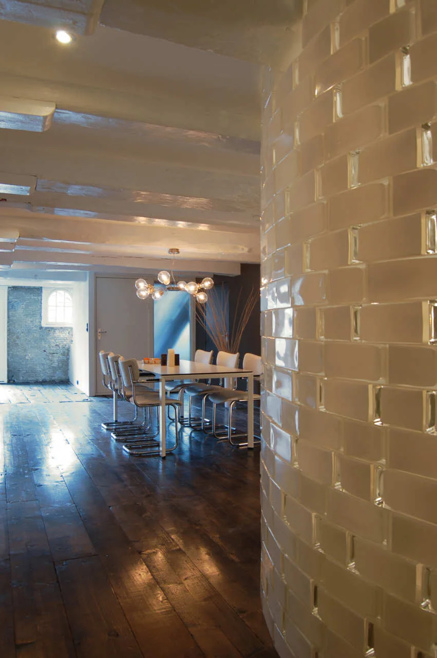 A dining room features a white table and chairs under a globe light fixture next to a curved white tiled wall and dark wood floors.