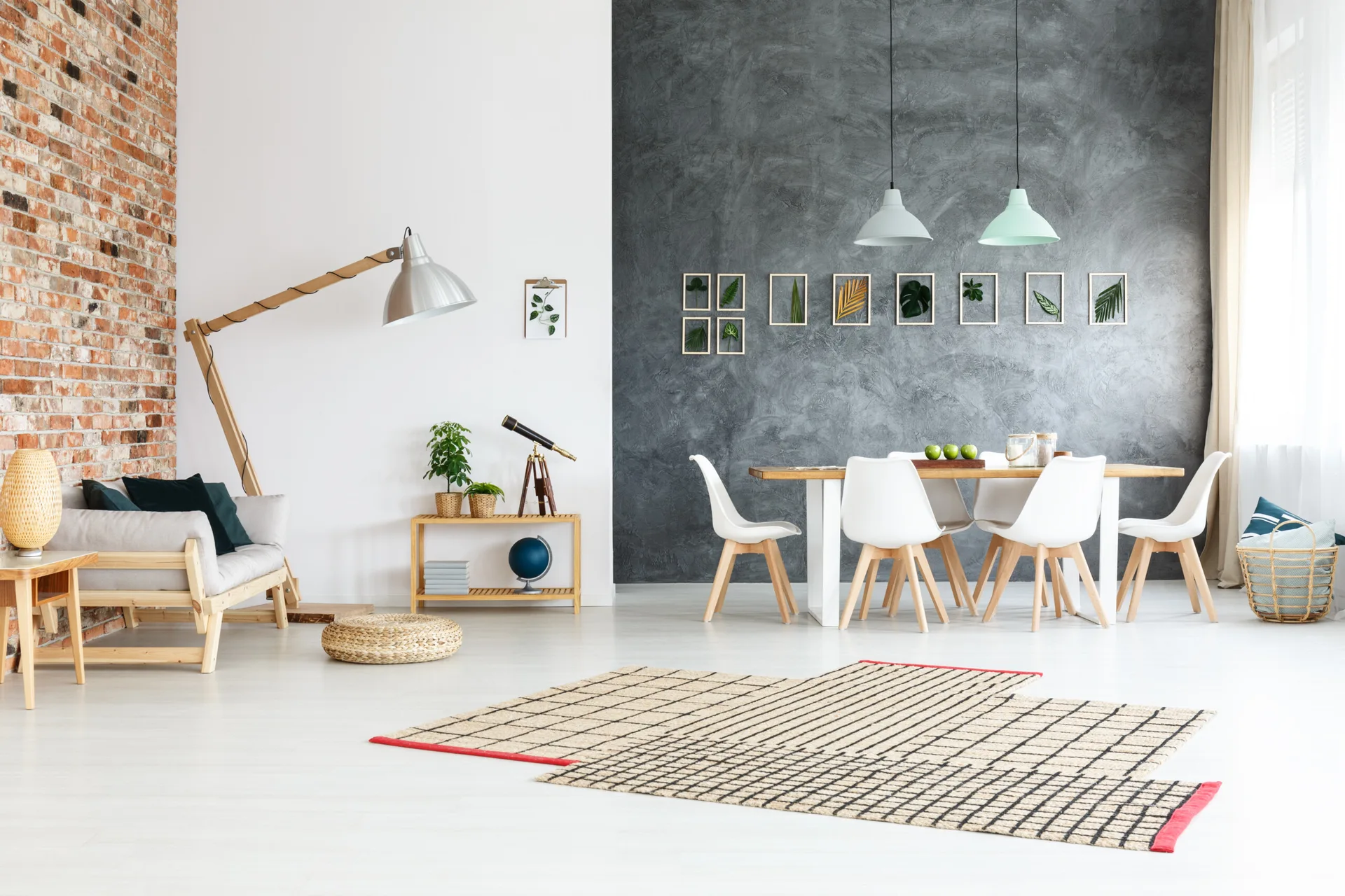 A spacious dining room featuring a wooden table with white chairs set against a grey textured wall, with an exposed brick wall in the living area.