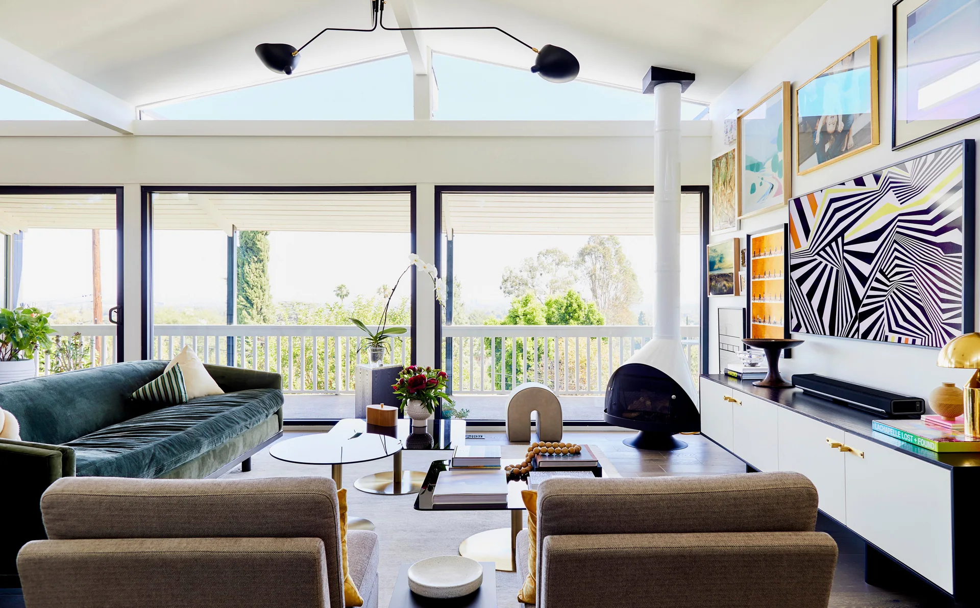 A bright living room features a green velvet sofa, a white conical fireplace, and large sliding glass doors leading to an outdoor deck.