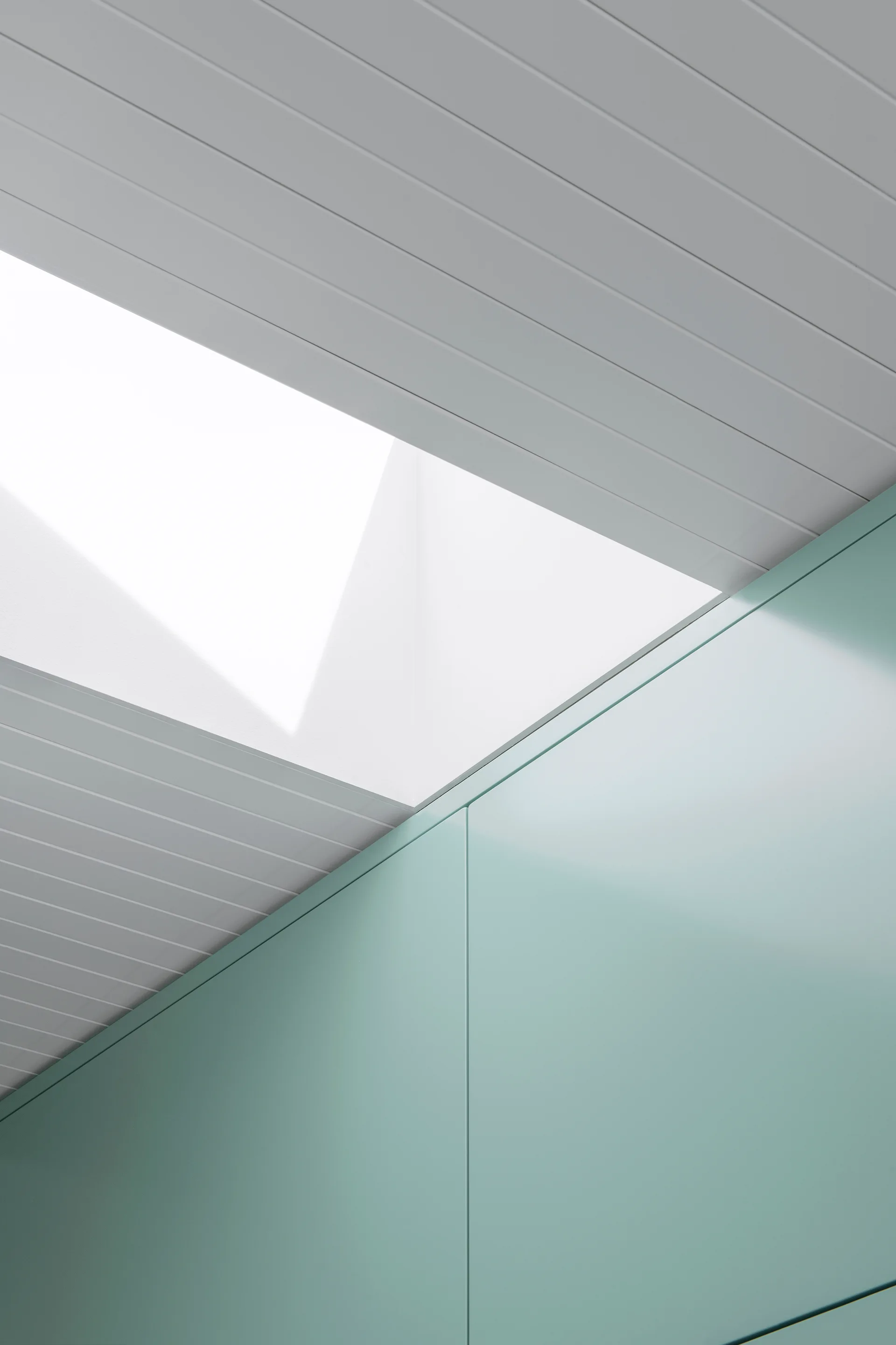 A close-up view of smooth mint green kitchen cabinetry beneath a white slatted wood ceiling featuring a recessed skylight cutout.