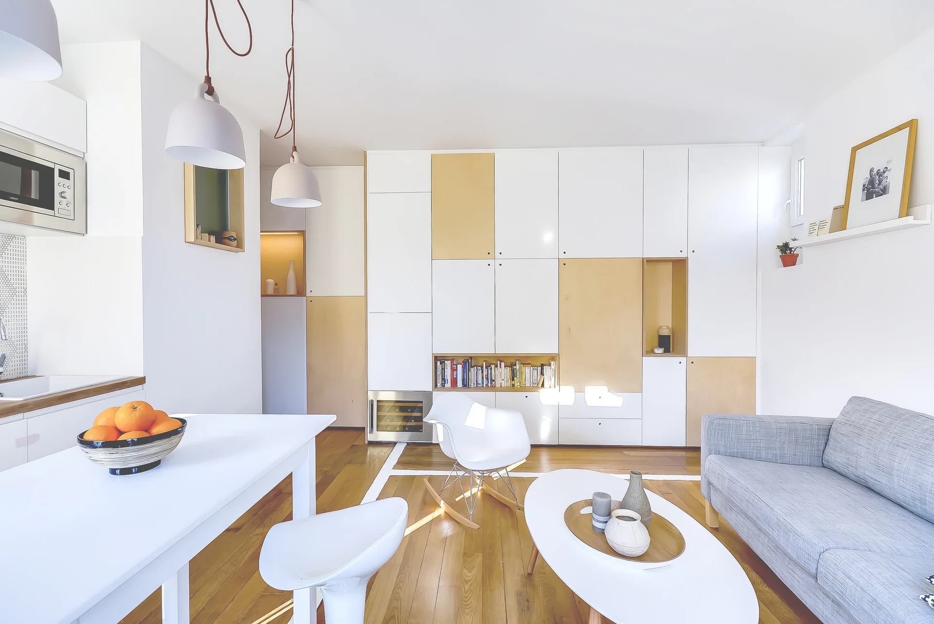 A bright living room features a white and light wood wall cabinet, a grey sofa, a white coffee table, and wood plank flooring.