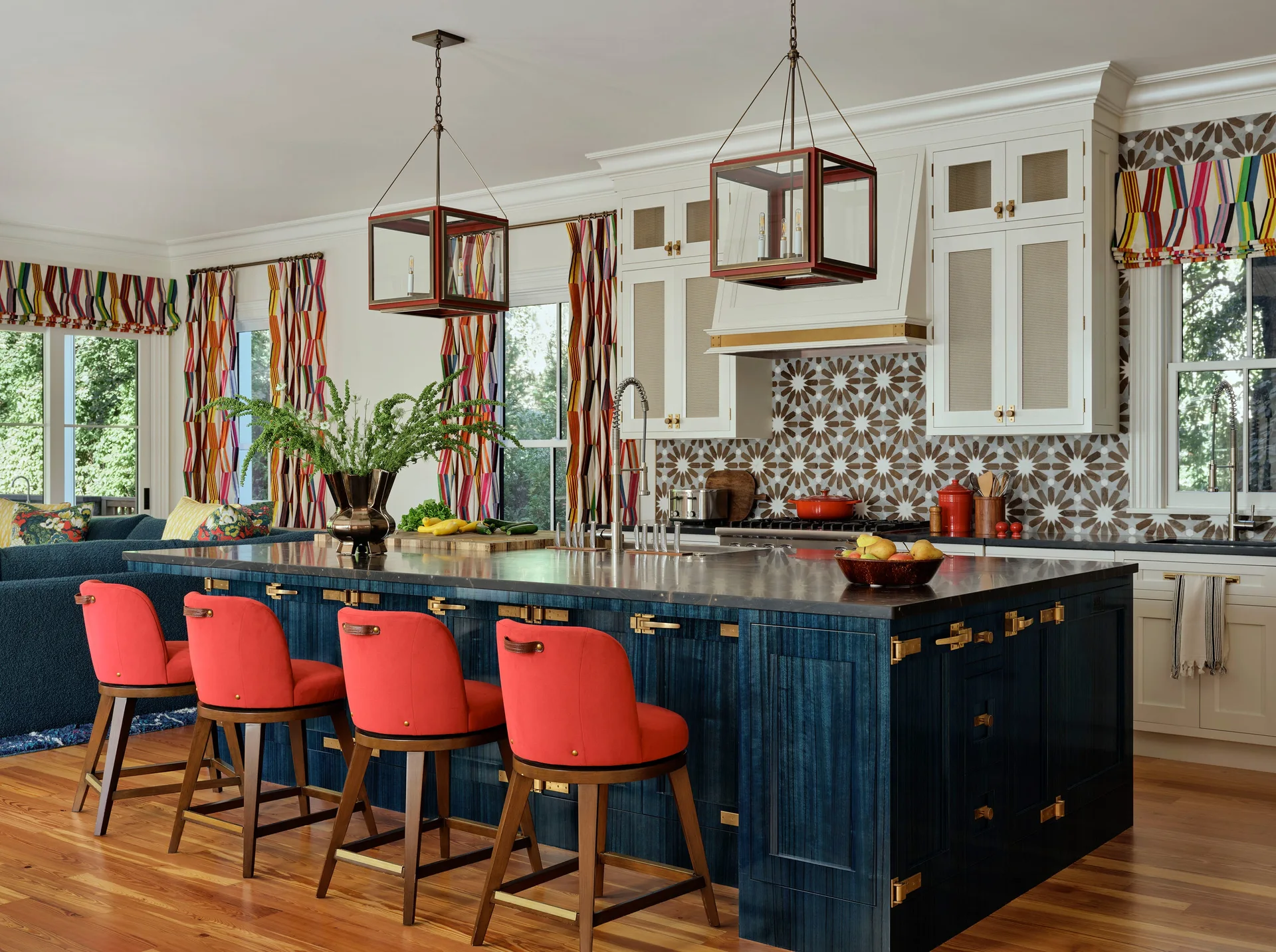 A kitchen featuring a large navy blue island with four red bar stools, white upper cabinets, and a starburst patterned tile backsplash.