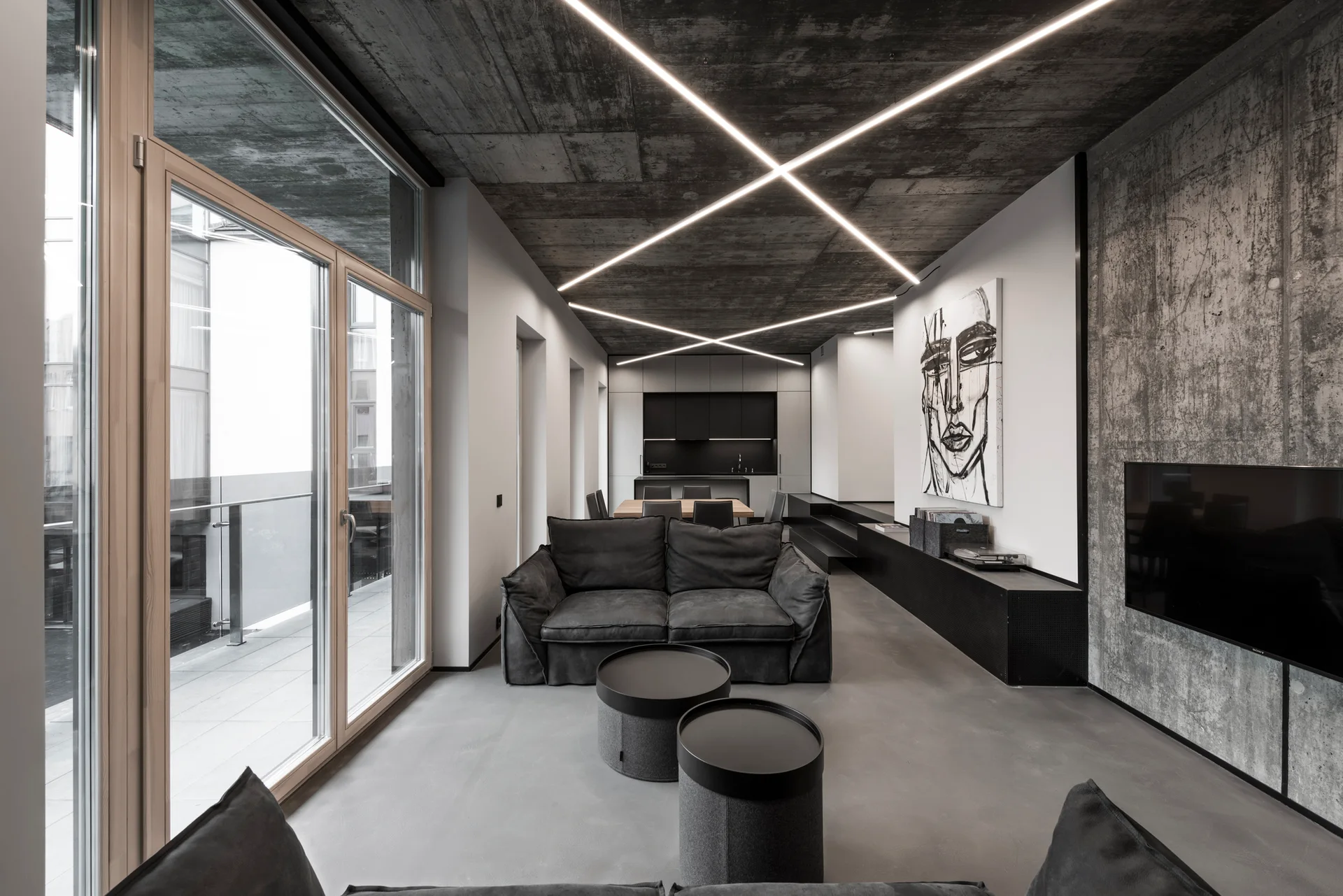 An industrial living room featuring an exposed concrete ceiling with crisscrossed linear lights, a grey fabric sofa, and sliding glass doors.