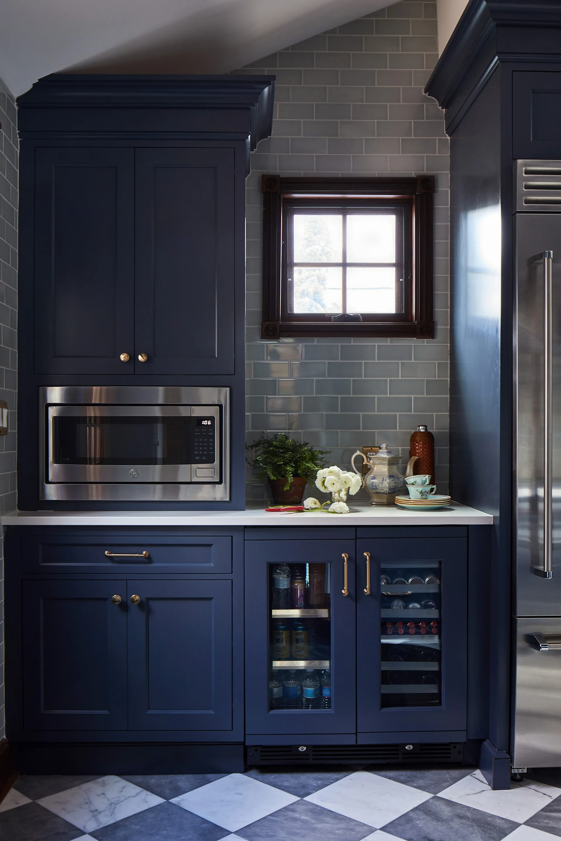 A kitchen pantry area features dark navy blue cabinetry, a gray subway tile backsplash, and checkered black and white floor tiles.