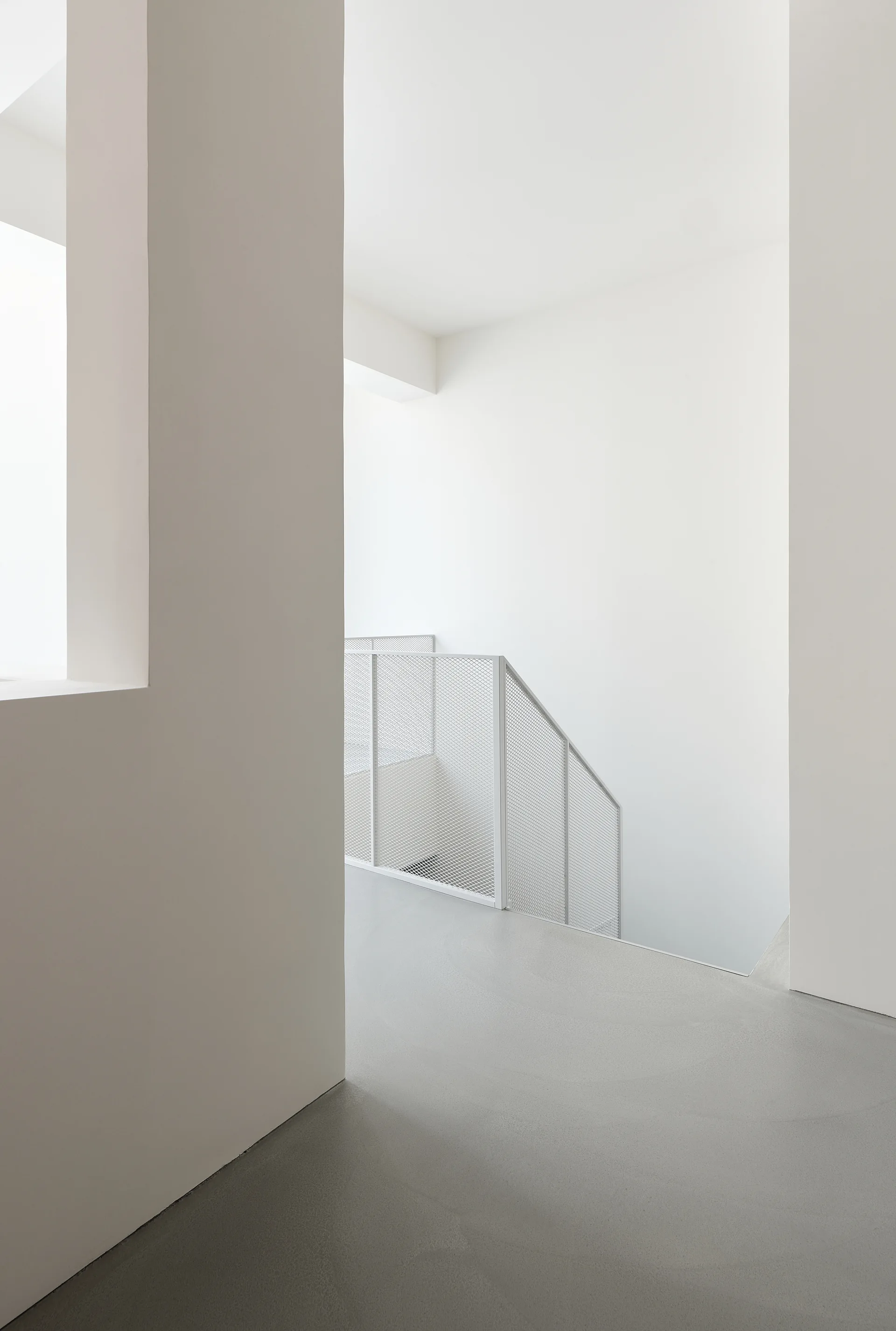 A minimalist white staircase features clean lines, a matte light gray floor, and a white metal mesh safety railing.