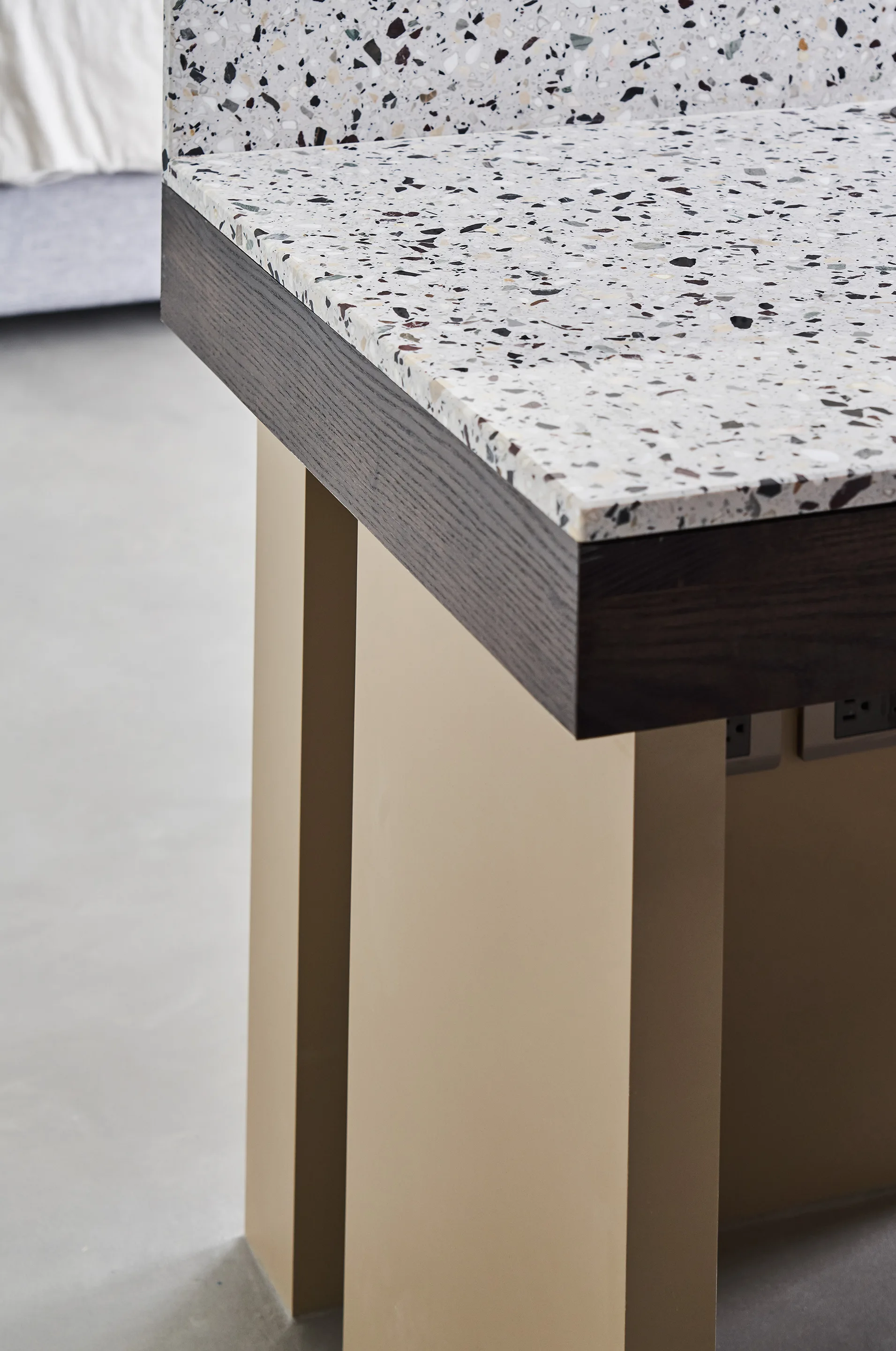 A close-up of a kitchen island featuring a speckled terrazzo countertop with dark wood trim on a tan base over a gray floor.