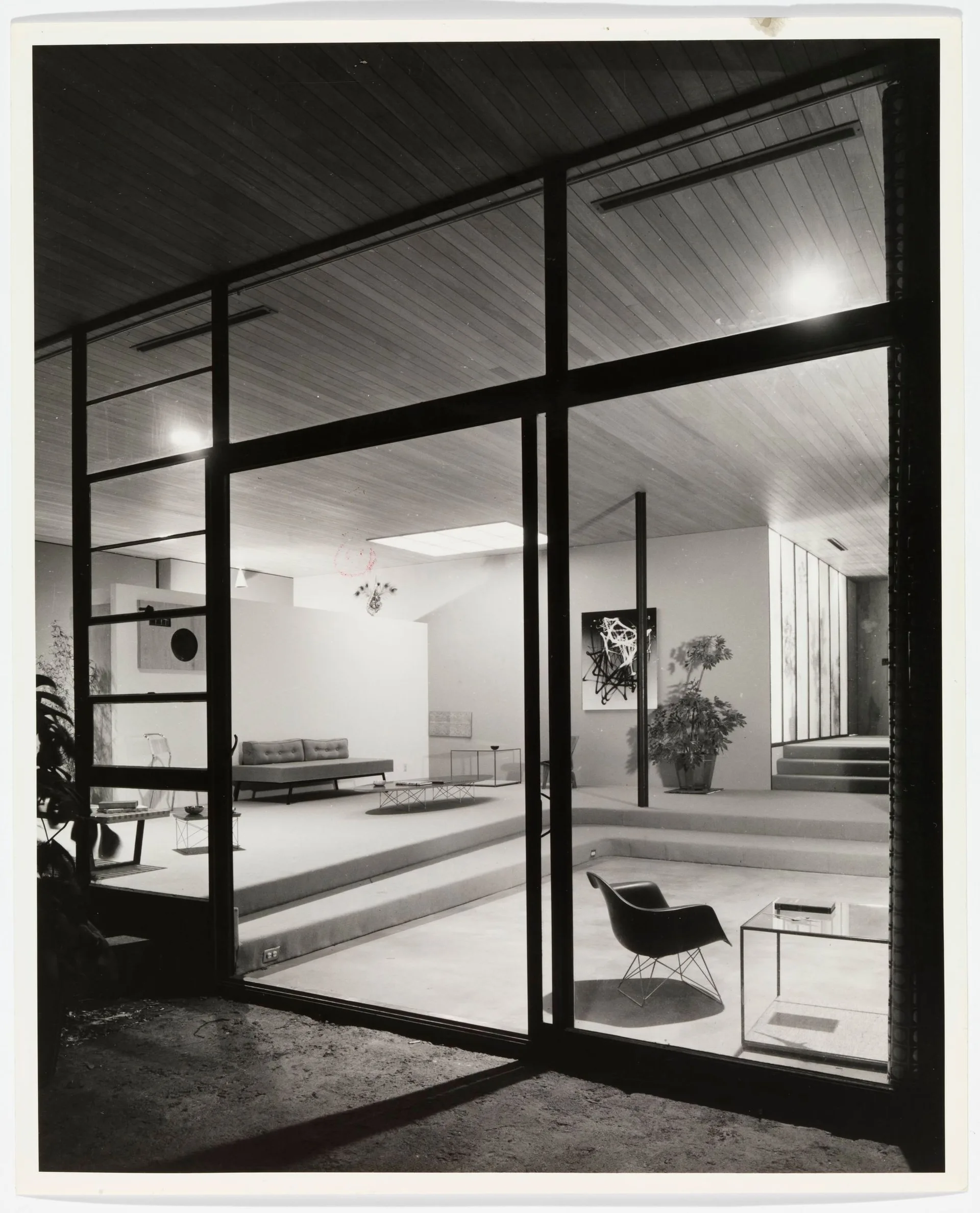 A mid-century modern living room with a sunken floor, a wood plank ceiling, large glass walls, minimalist furniture, and a skylight.