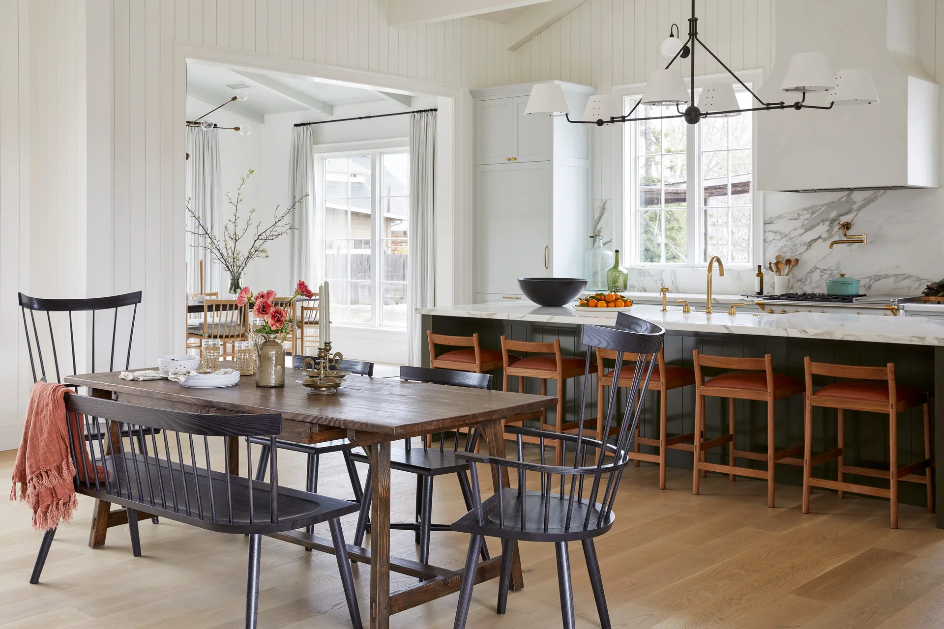 An open kitchen and dining area features a dark wood dining table with black spindle chairs next to a marble-topped kitchen island.