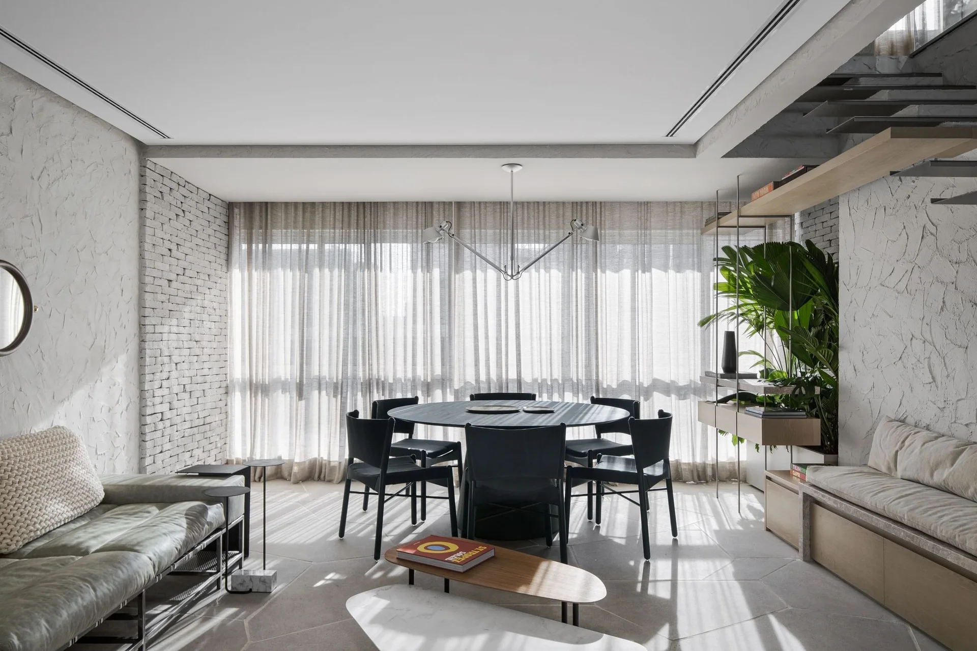 A modern dining room features a black circular table with matching chairs, set on hexagonal stone floor tiles next to textured plaster and brick walls.
