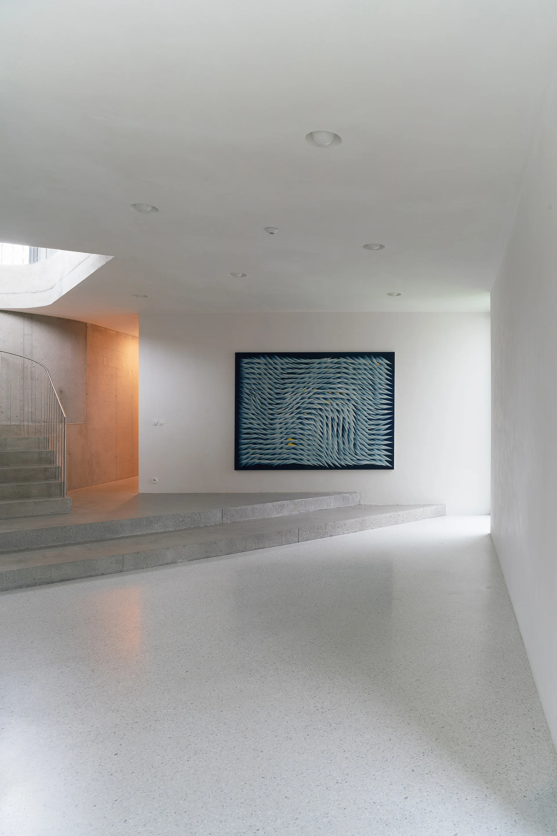 A minimalist entryway featuring polished grey terrazzo flooring, raw concrete steps, and a large blue abstract painting on a white wall.