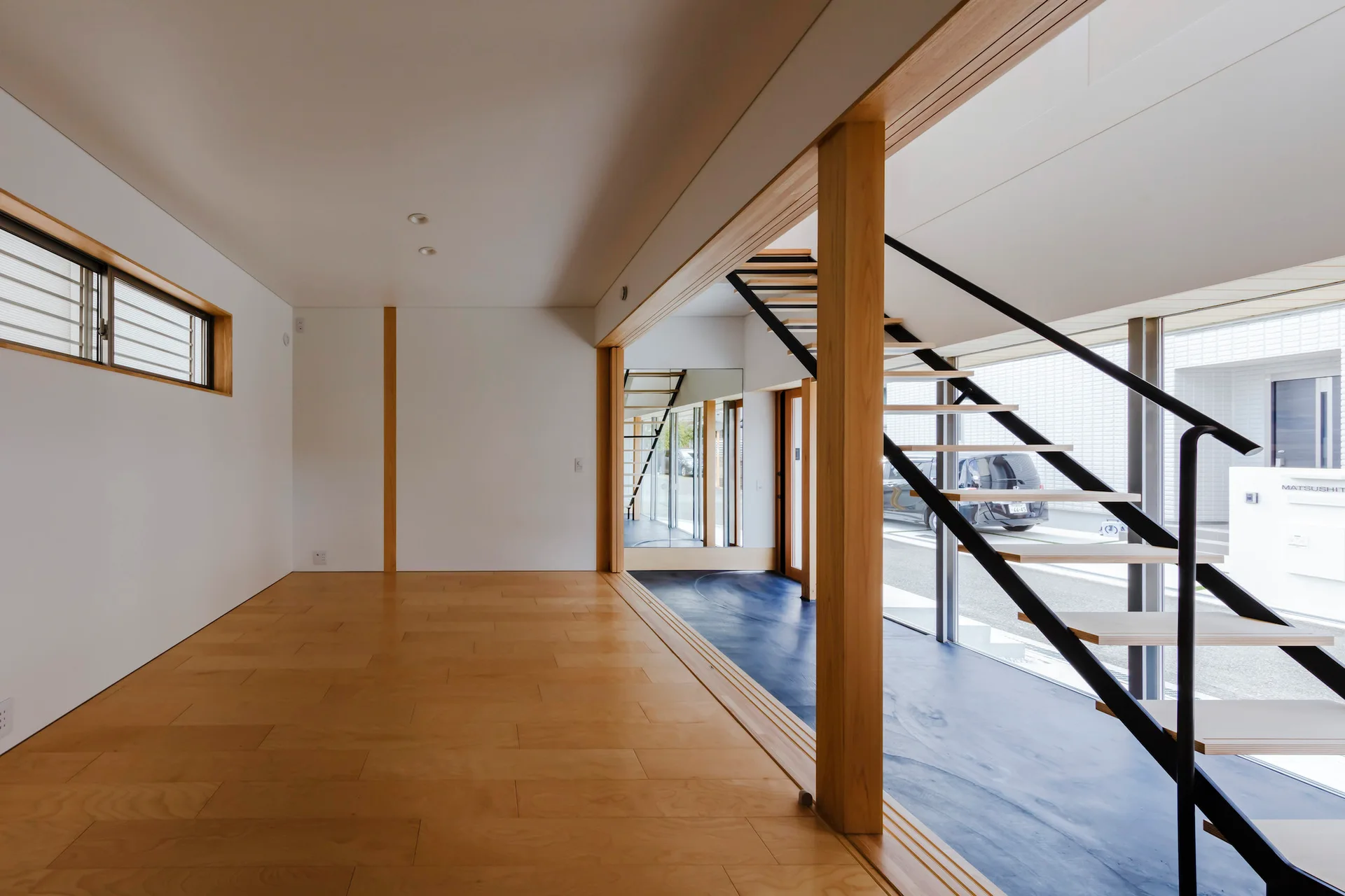 A minimalist modern room featuring light wood floors, white walls, and an open-riser staircase with wooden treads and a black metal railing.