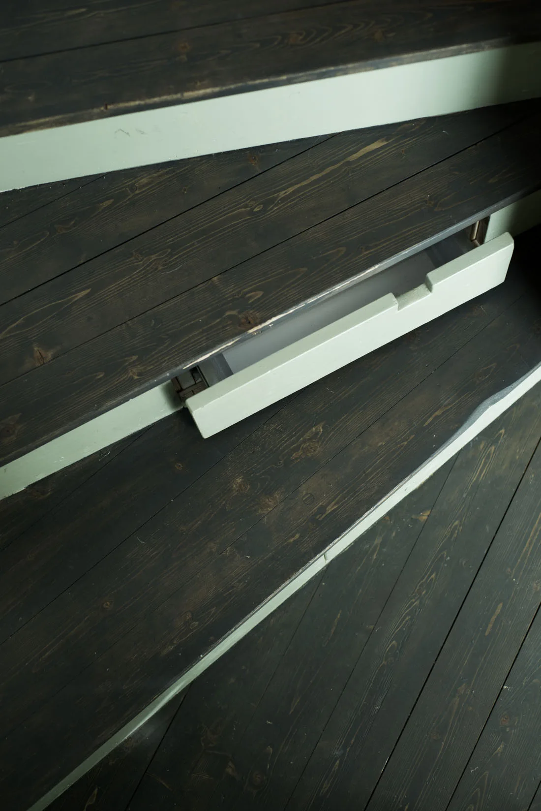 A close-up of dark wood staircase treads with a sage green riser featuring a partially open built-in drawer.