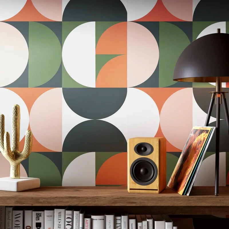 A wooden shelf holds a small speaker, a gold cactus sculpture, and a black tripod lamp against a background of colorful geometric circle wallpaper.
