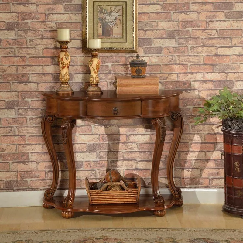 A traditional dark wood demilune console table with curved legs stands against an exposed brick wall, decorated with candlesticks and a framed picture.
