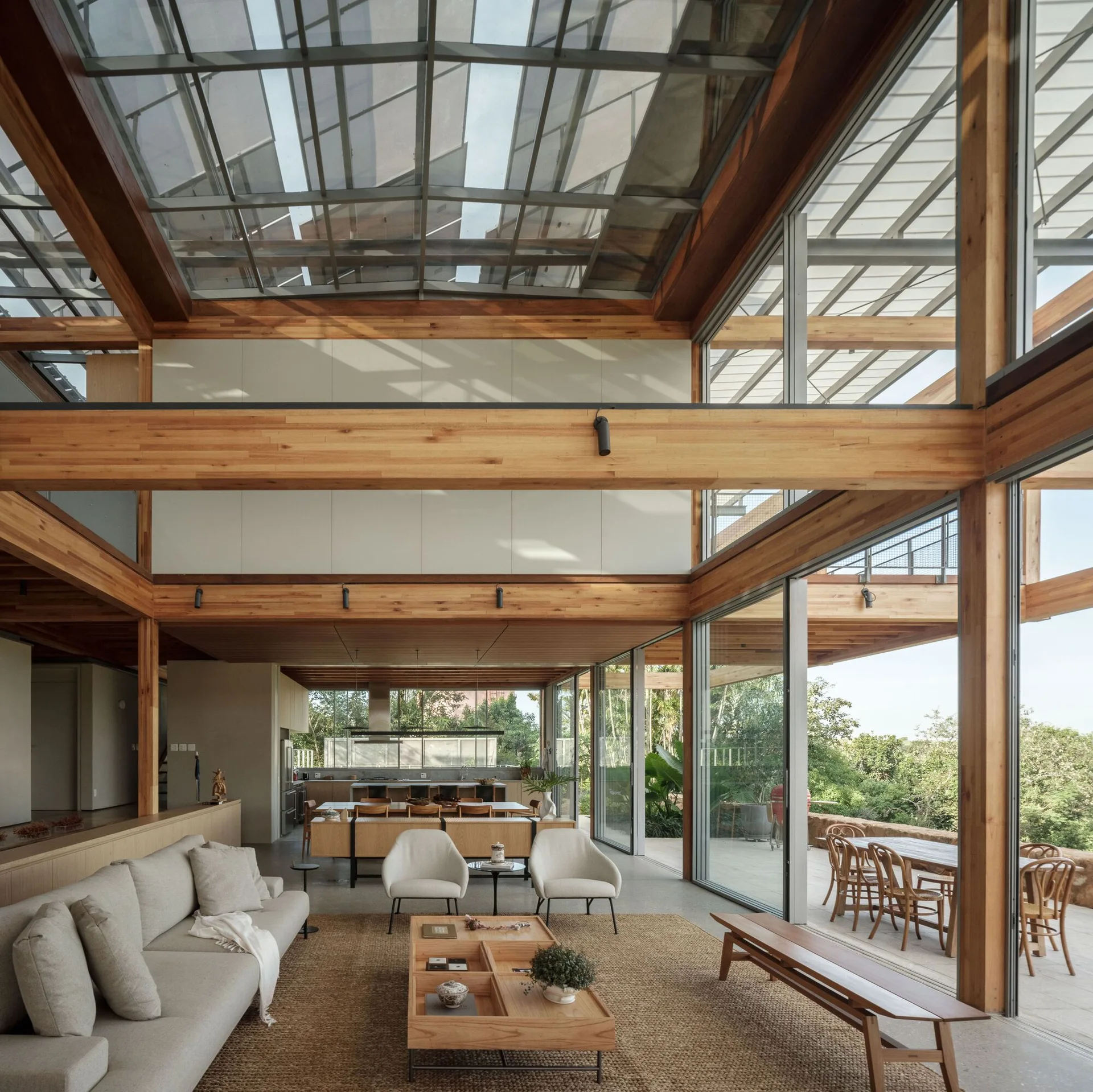 An open-concept living room features a beige sofa, a low wooden coffee table, and an expansive glass skylight supported by heavy timber beams.