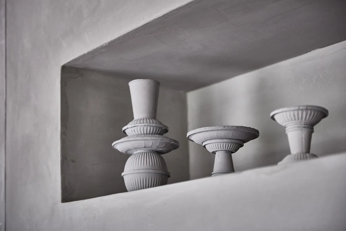 Three matte gray ceramic vessels with ribbed textures are displayed inside a recessed plaster wall niche with soft shadows.