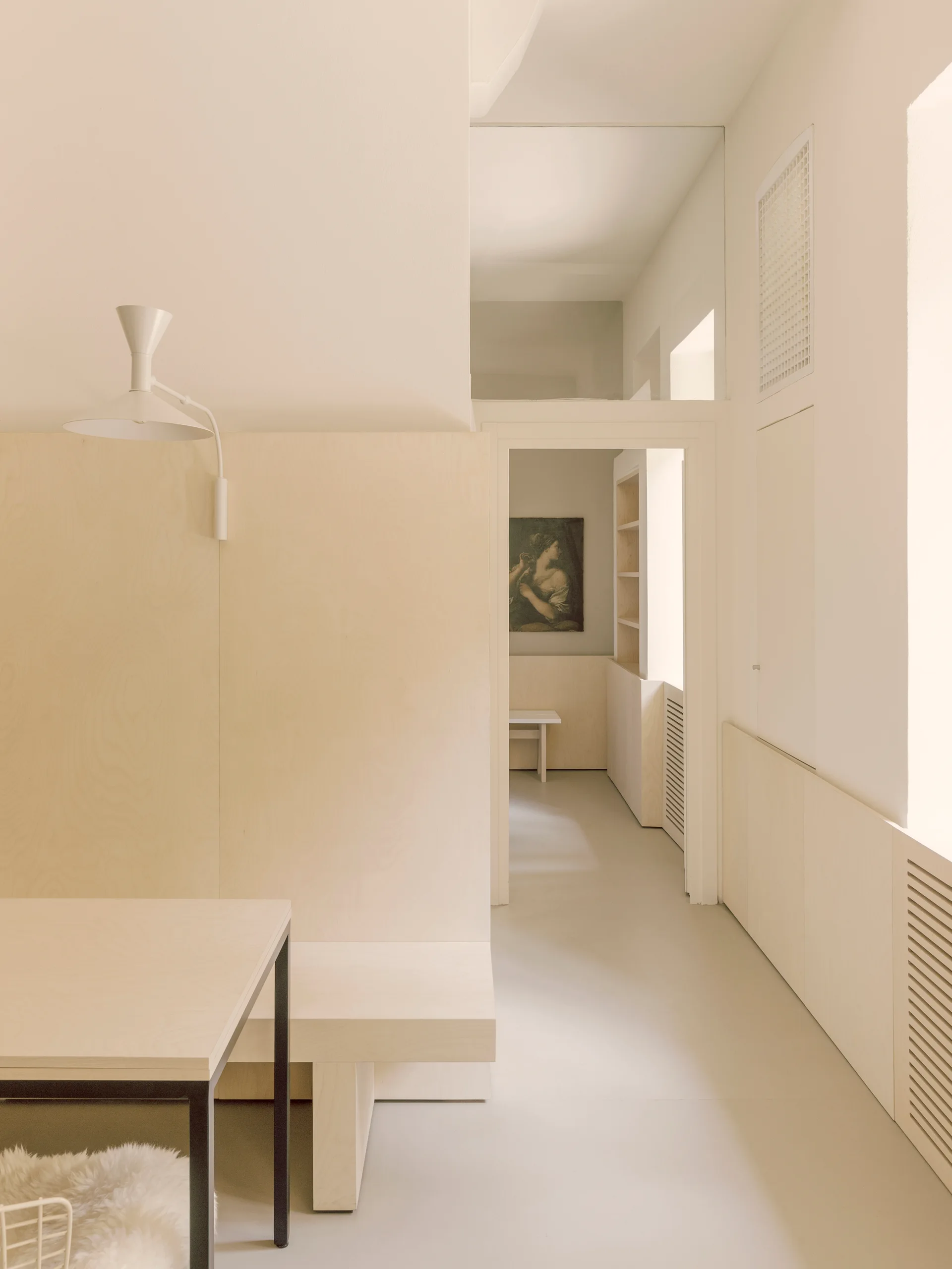 A minimalist dining space features light plywood wall paneling, an integrated bench, and a matching wood table under soft ambient light.