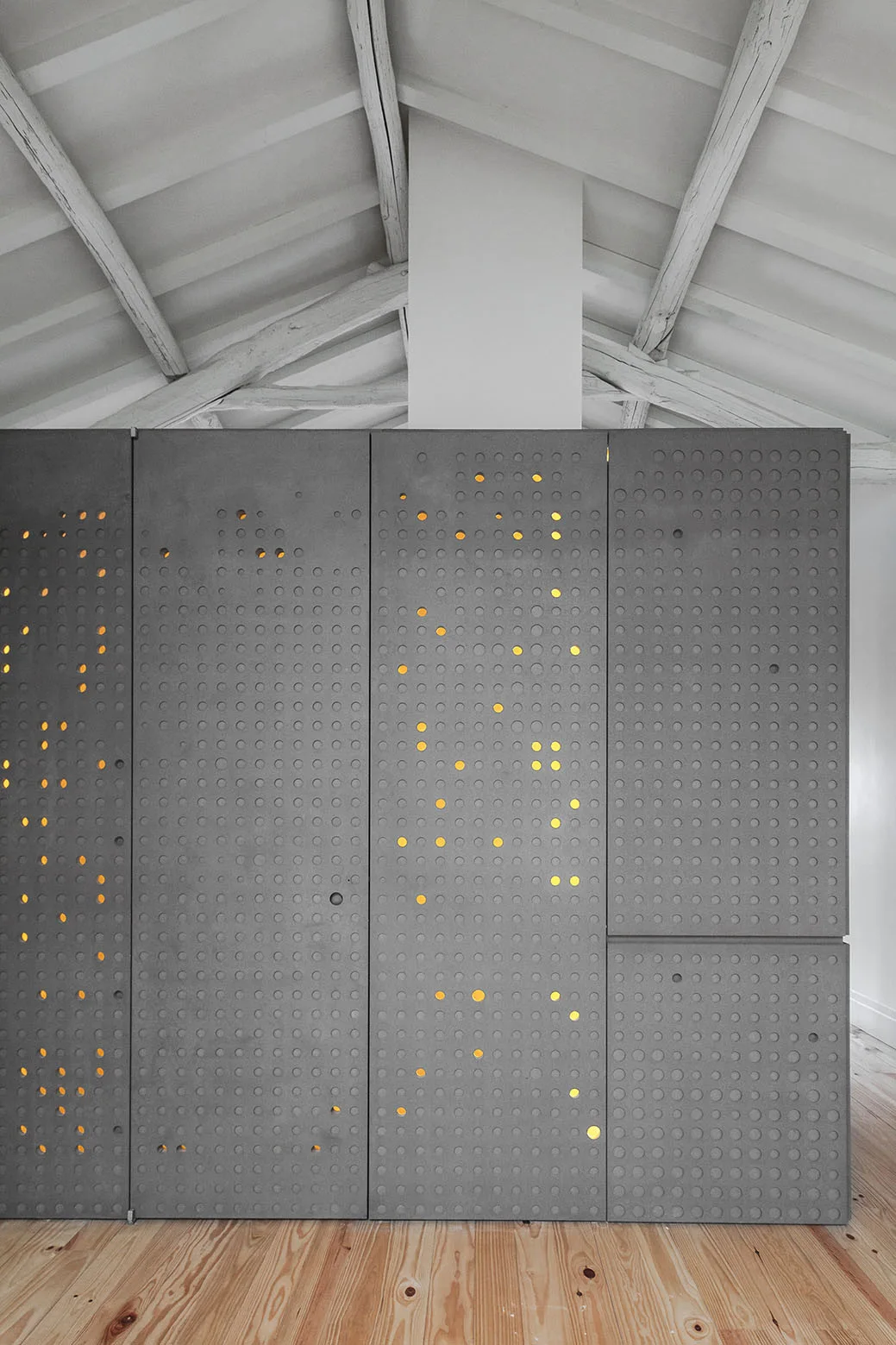 A large grey perforated storage cabinet glows with integrated backlighting beneath a white exposed beam ceiling and above natural wood floors.