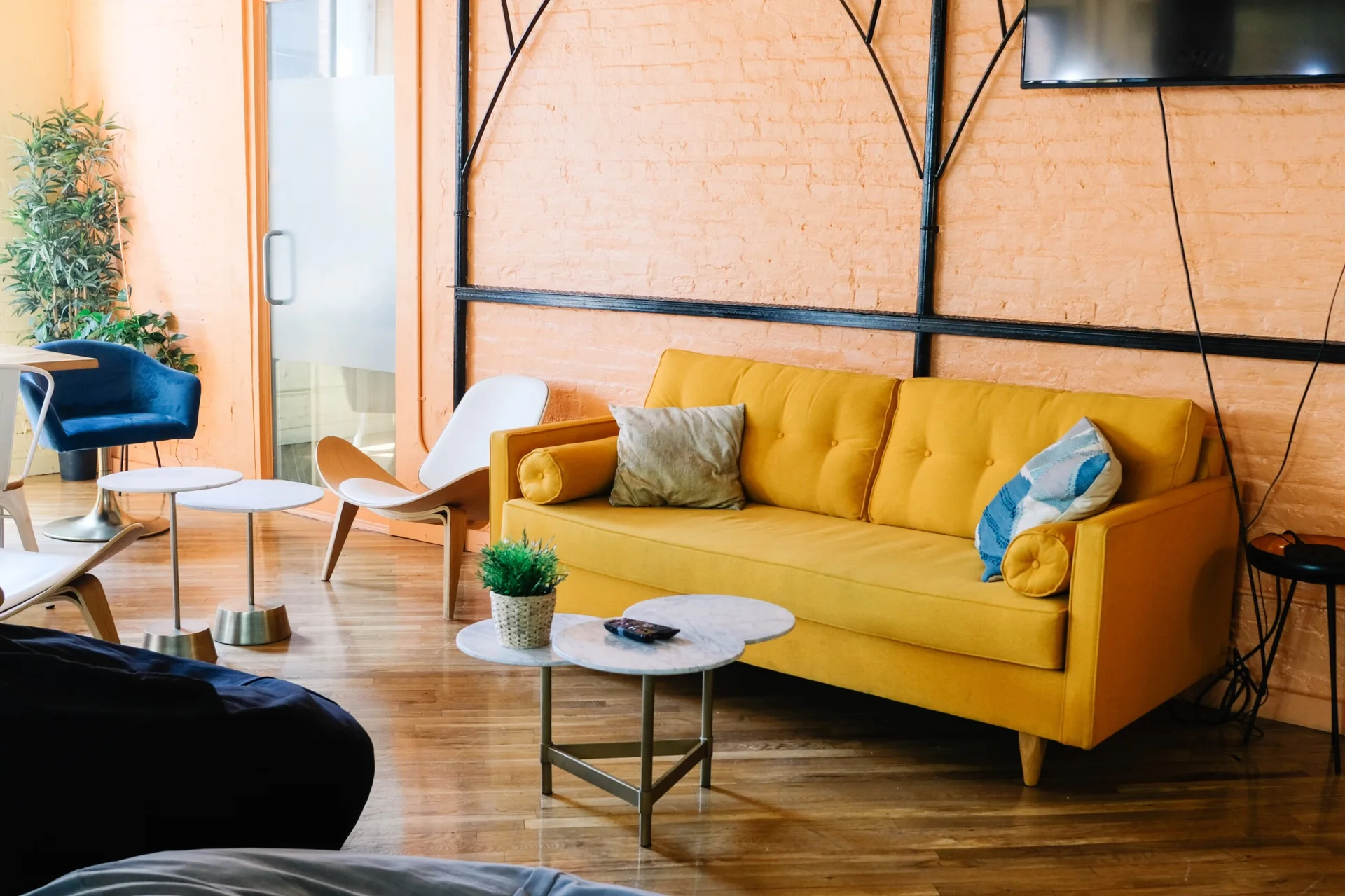 A bright yellow sofa sits against a painted orange brick wall next to nested marble coffee tables in a room with hardwood flooring.