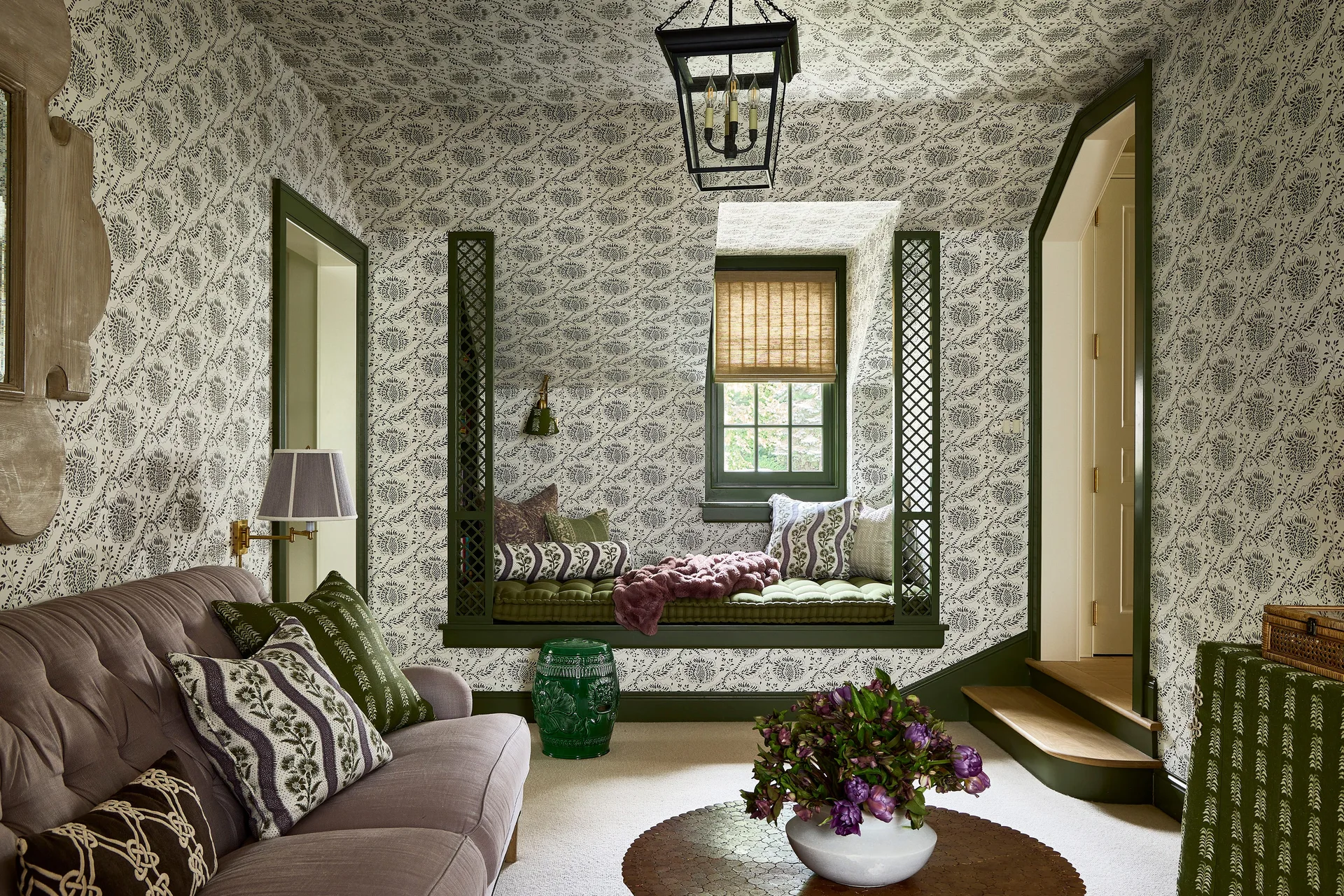 A cozy living room features walls and ceiling wrapped in botanical wallpaper, a mauve sofa, and a green-framed built-in window seat nook.