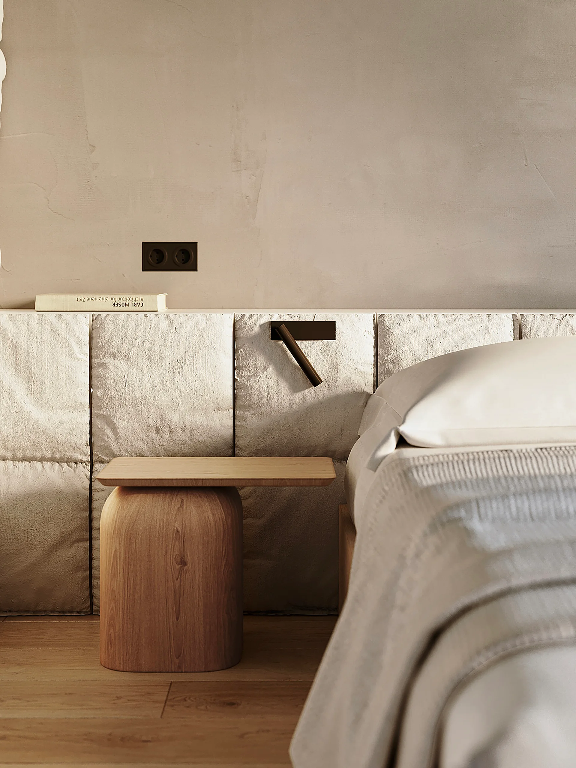 A close-up of a bed with white linens next to a curved wood nightstand against a textured stone block headboard wall.