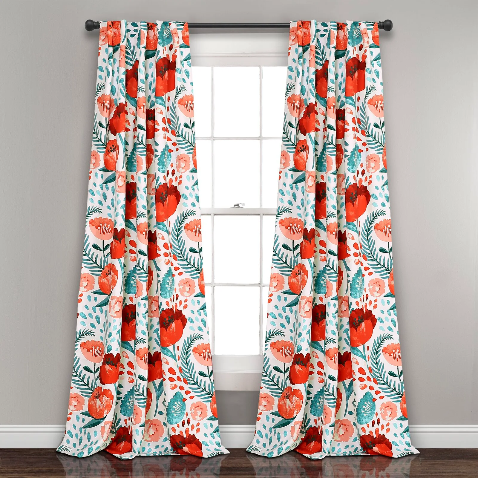 A pair of white curtains with a red and teal floral pattern hang from a black metal rod in front of a white window.