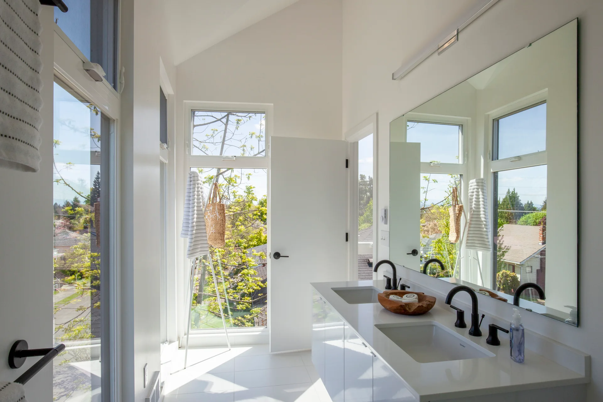A bright modern bathroom features a white double vanity with matte black faucets, a large mirror, and high vaulted ceilings.